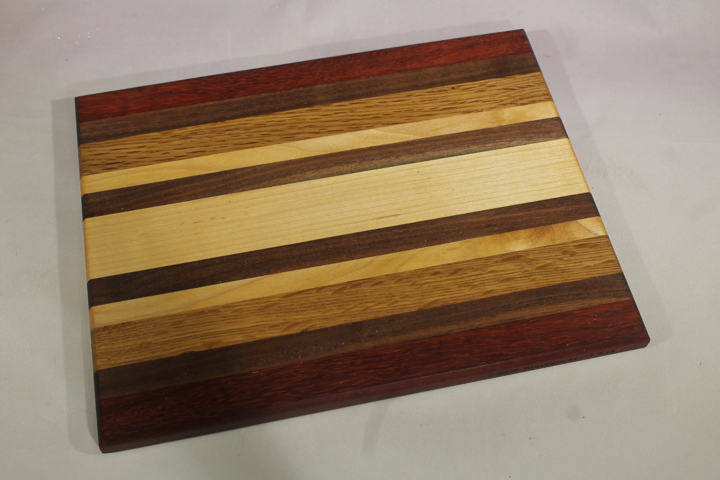 CB48  -  Charcuterie board           $70

7 ¼” wide by 9 ¼” long by 11/16” thick.
Thirteen segments of wood – Paduk, Walnut, Oak, Maple, Walnut, Maple, Walnut, Maple, Walnut, Maple, Oak, Walnut, Paduk.

Finished with cutting board oil.
