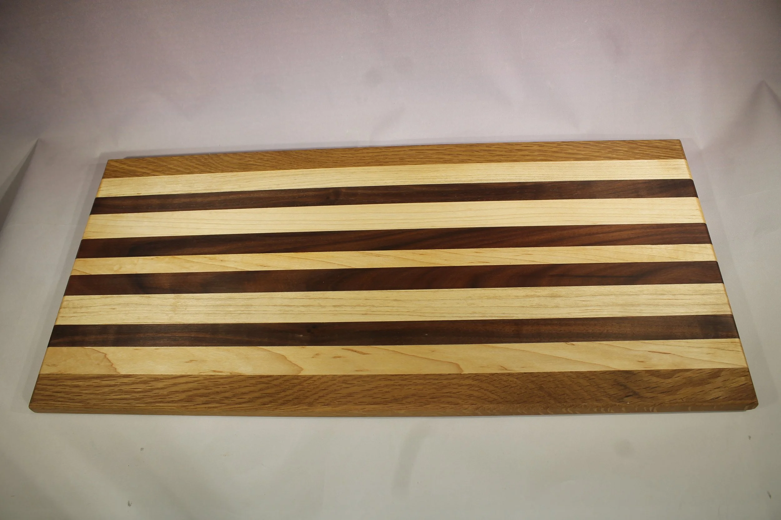 CB57 -  Charcuterie board.

9 ¼” wide by 20” long by ¾” thick.
Eleven segments of wood – Oak, Maple, Walnut, Maple, Walnut, Maple, Walnut, Maple, Walnut, Maple, Oak.

Finished with cutting board oil.       $80
