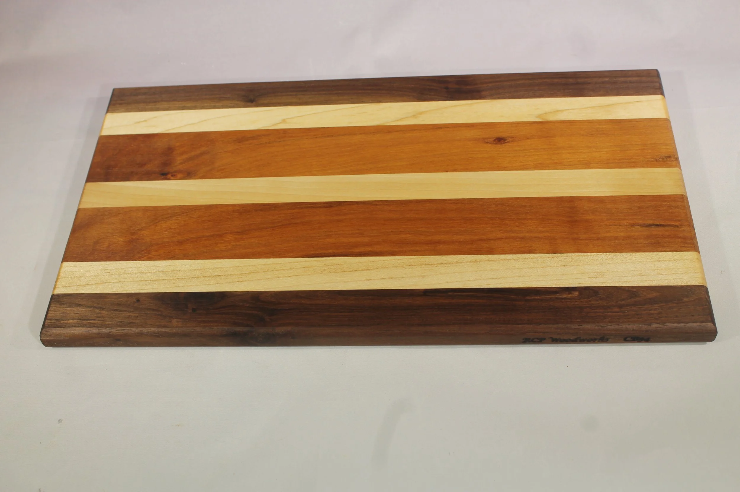 CB54 - Charcuterie board.            $70

13 ½” long x 7 ⅝” wide x ⅝” thick.
Seven segments of wood – Walnut, Maple, Bubinga, Walnut, Bubinga, Maple, Walnut.

Finished with cutting board oil            