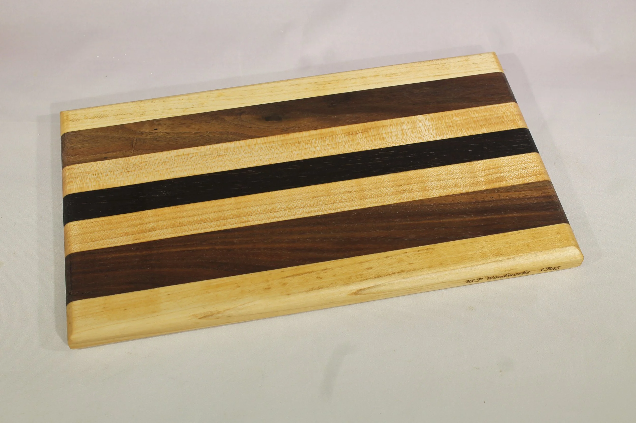 CB45 -  Cheese & Cutting board         $55

6 1/8” wide by 10 ¾” long by 11/16” thick.
Seven segments of wood – Maple, Walnut, Maple, Wenge, Maple, Walnut, Maple.

Finished with cutting board oil.
