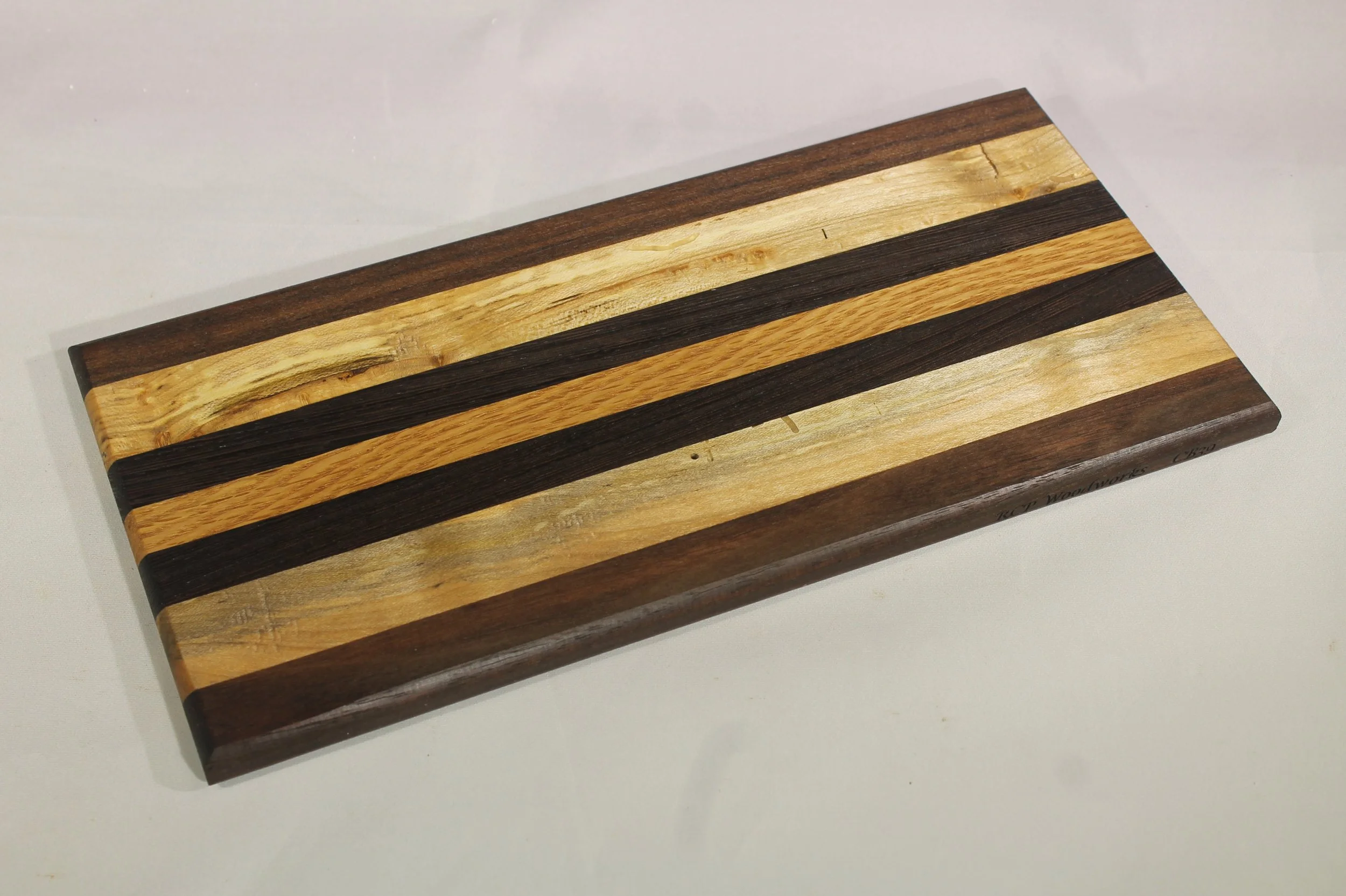 CB 39A - Cheese & Cutting board.

5 ¼” wide by 11 3/8” long by 5/8” thick.
Seven segments of wood – Walnut, Maple,  Wenge, Oak, Wenge, Maple, Walnut

Finished with cutting board oil.         $50
