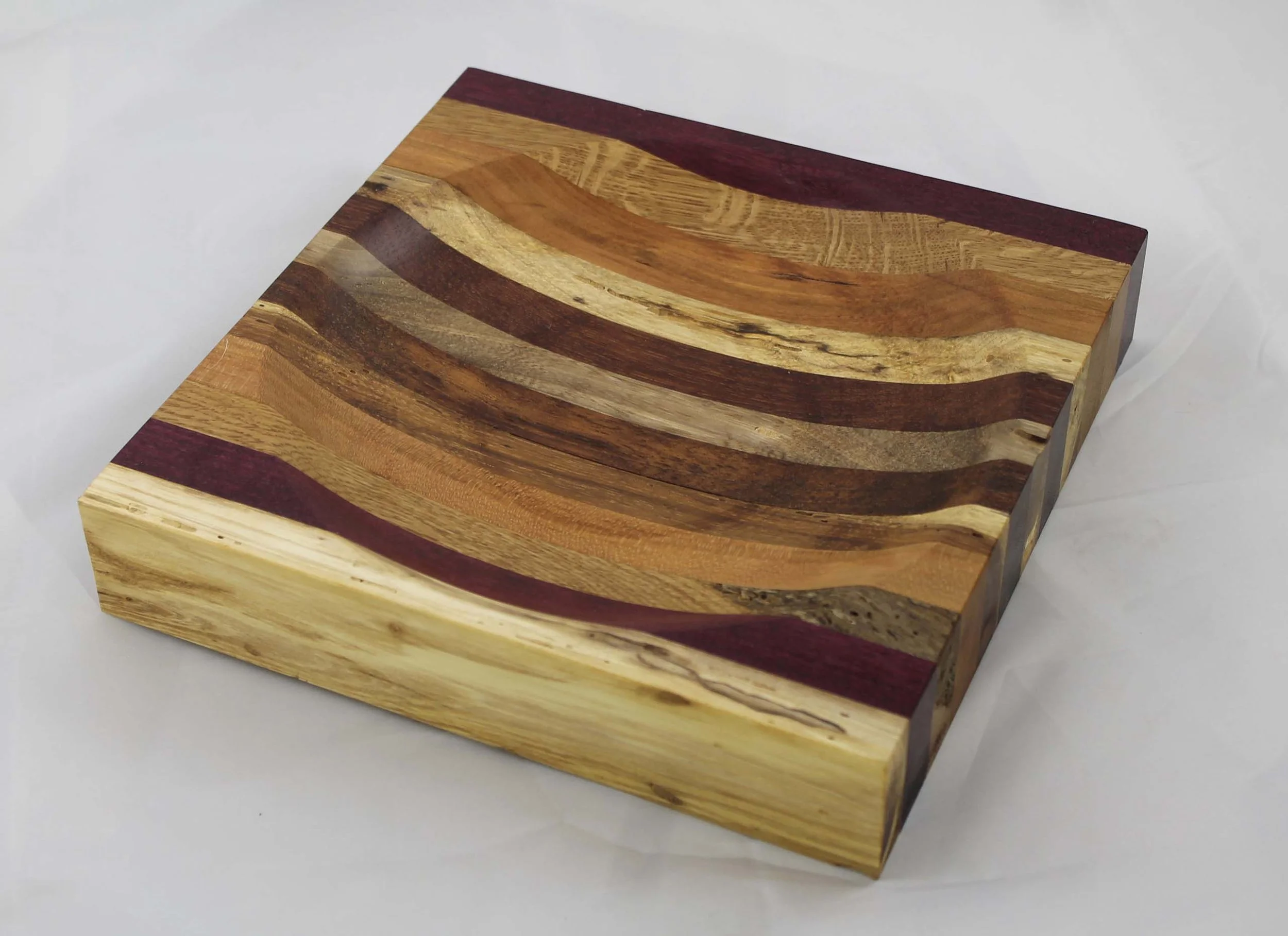 CB28 - Ulu knife cutting board.  
This cutting board measures 9”W x 9”L x 1⁵⁄₈” H.  
It has12 segments – Pecan / Purpleheart / Oak / Cherry / Walnut / Jatoba / Elm / Jatoba / Walnut / Cherry / Oak / Purpleheart.
$45