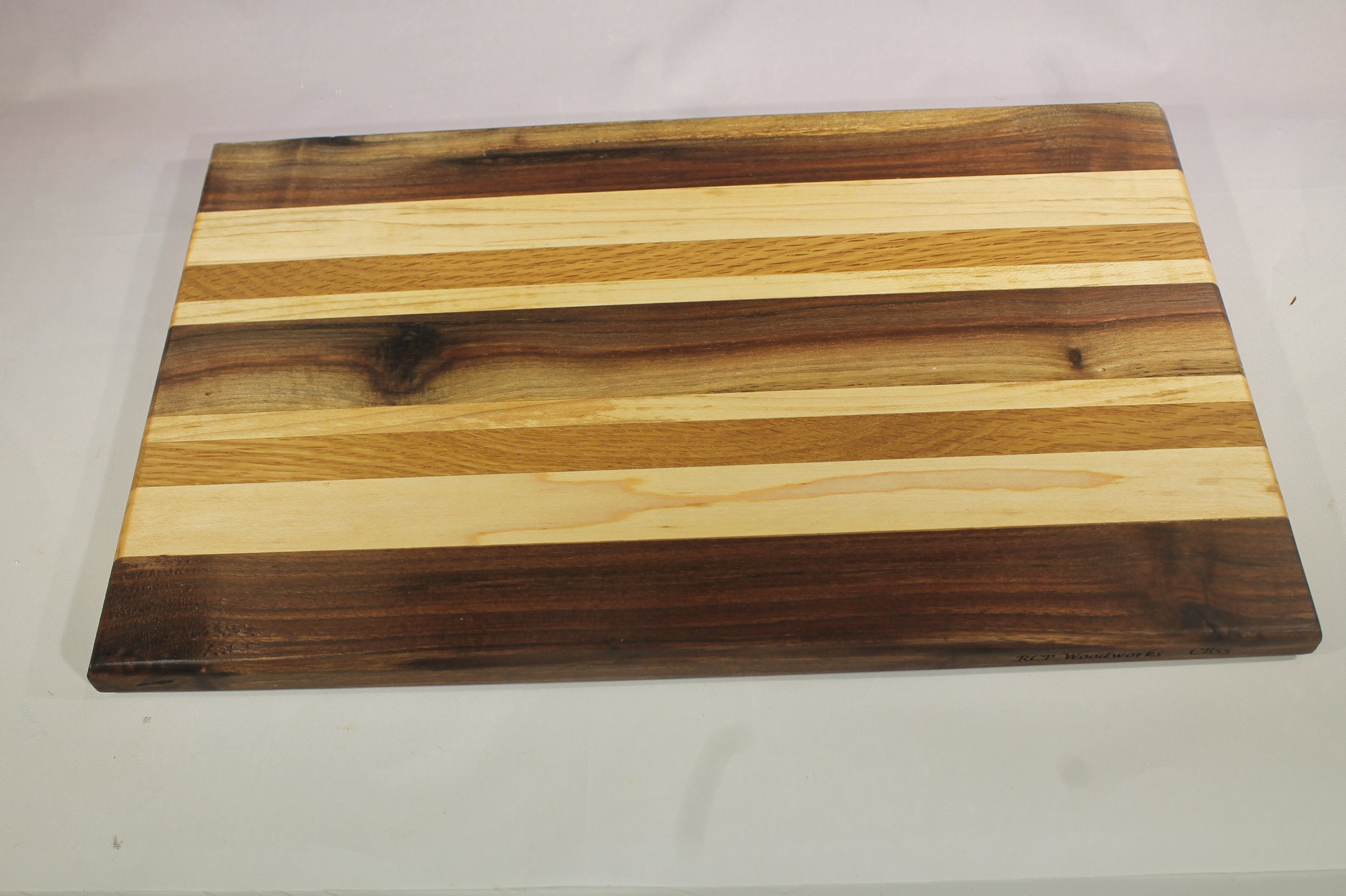 CB55 - Charcuterie board.

8 ¾” wide by 14” long by ¾” thick.
Nine segments of wood – Walnut, Maple, Oak, Maple, Walnut, Maple, Oak, Maple, Walnut.

Finished with cutting board oil.       $75
