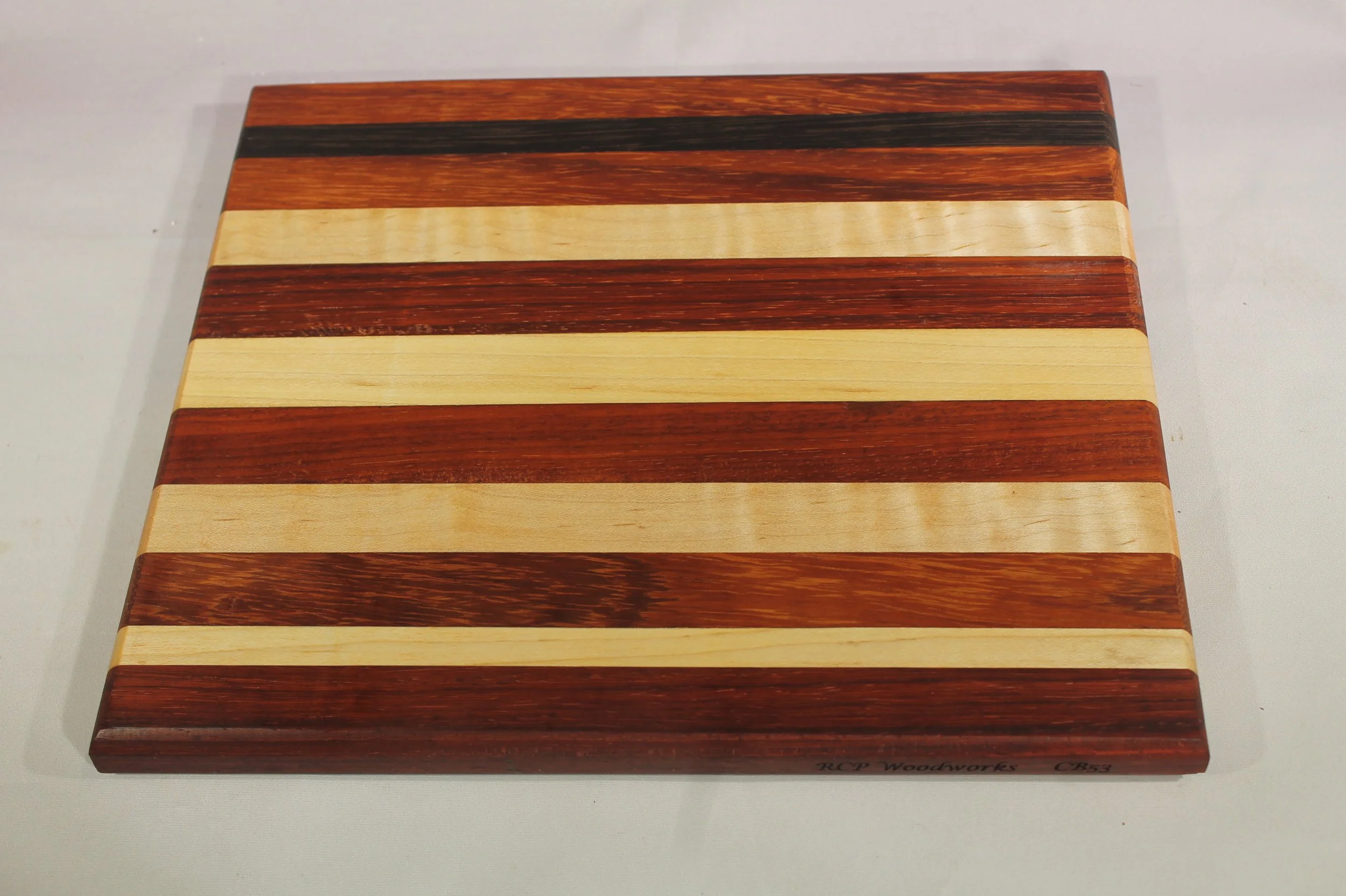 CB53 - Charcuterie board.

8 ¼” wide by 9 3/8” long by 11/16” thick.
Eleven segments of wood – Paduk, Maple, Bubinga, Maple, Paduk, Maple, Paduk, Maple, Paduk, Wenge, Paduk.

Finished with cutting board oil.       $80
