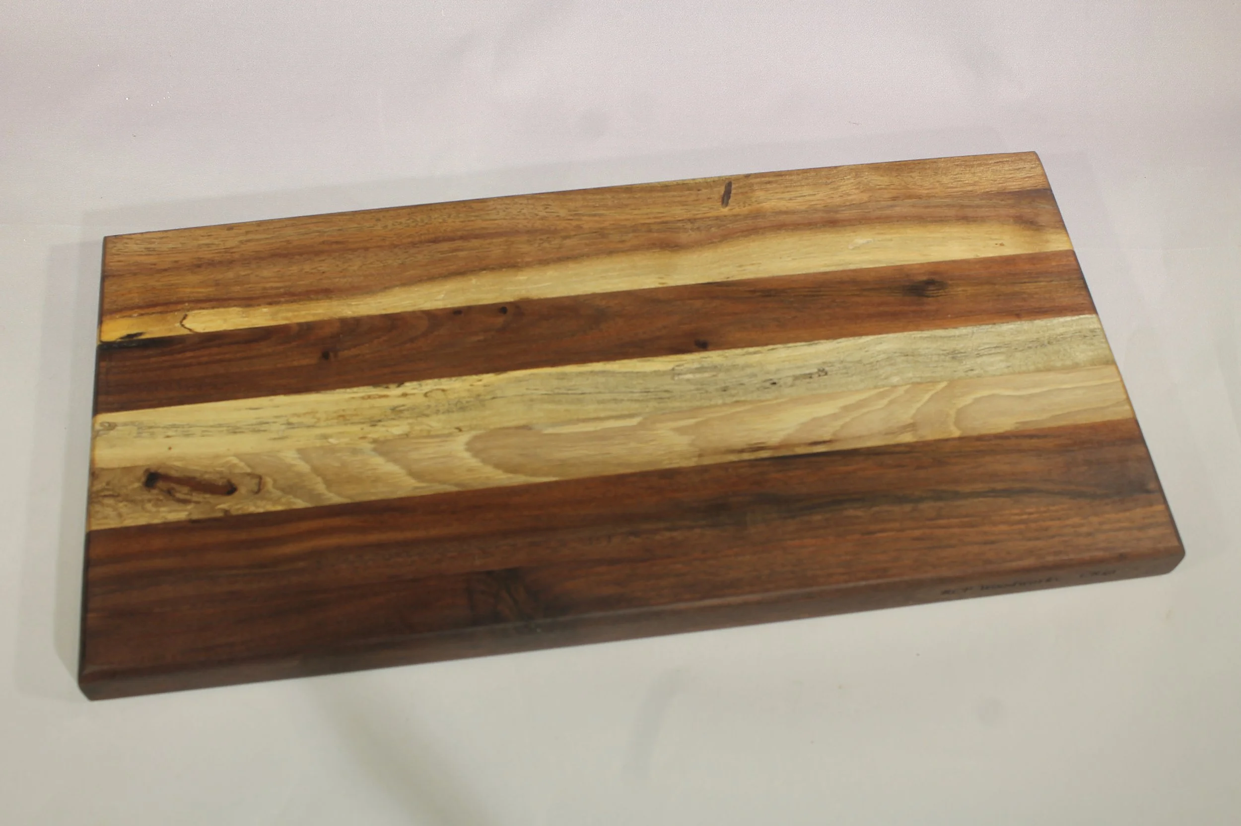 CB49 -  Charcuterie board.

6” wide by 12 ¼” long by 7/8” thick.
Seven segments of wood – Walnut, Walnut, Maple, Cherry, Walnut, Walnut, Walnut.

Finished with cutting board oil.       $60
