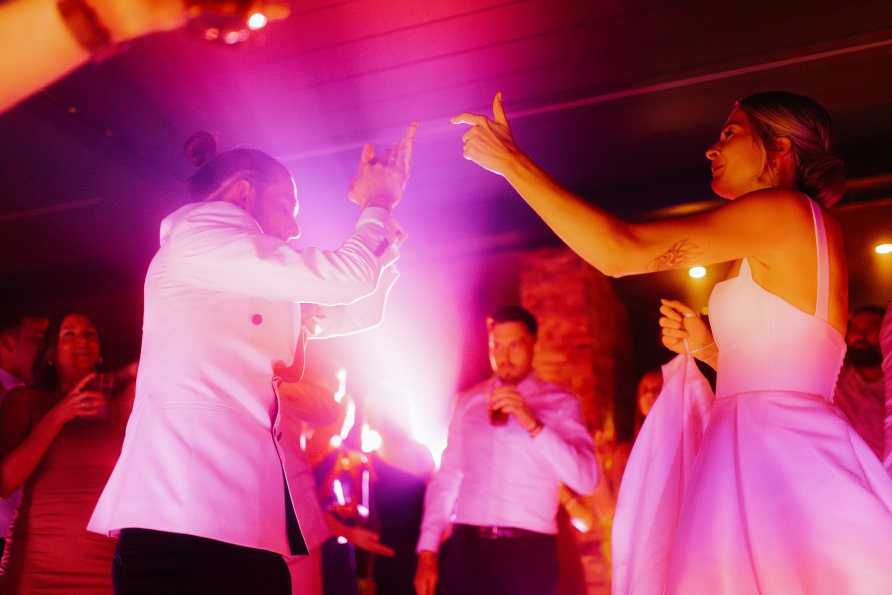 Zwei Frauen tanzen auf einer Party bei rotem und pinkem Licht, umgeben von anderen Gästen.