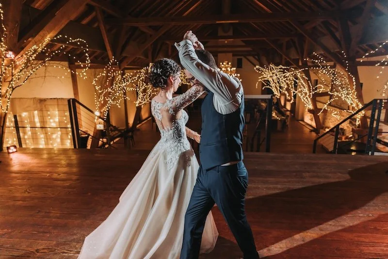 Braut und Bräutigam tanzen auf einer Hochzeit in einem festlich dekorierten Saal mit Lichterketten und dekorativen Bäumen.