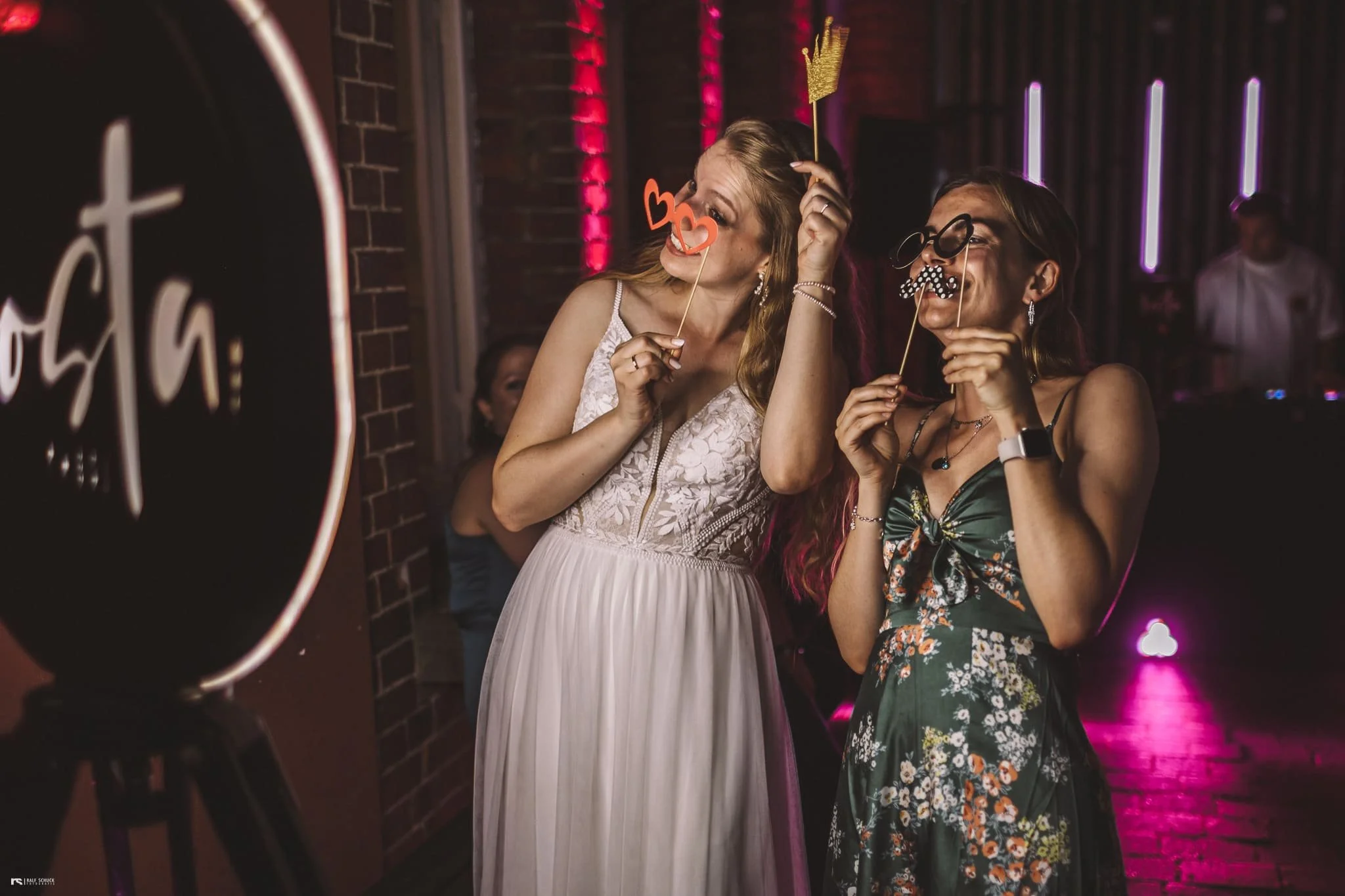 Zwei Frauen auf einer Party mit lustigen Accessoires wie Brillen, Schnurrbärten und Herzen, die Spaß haben.