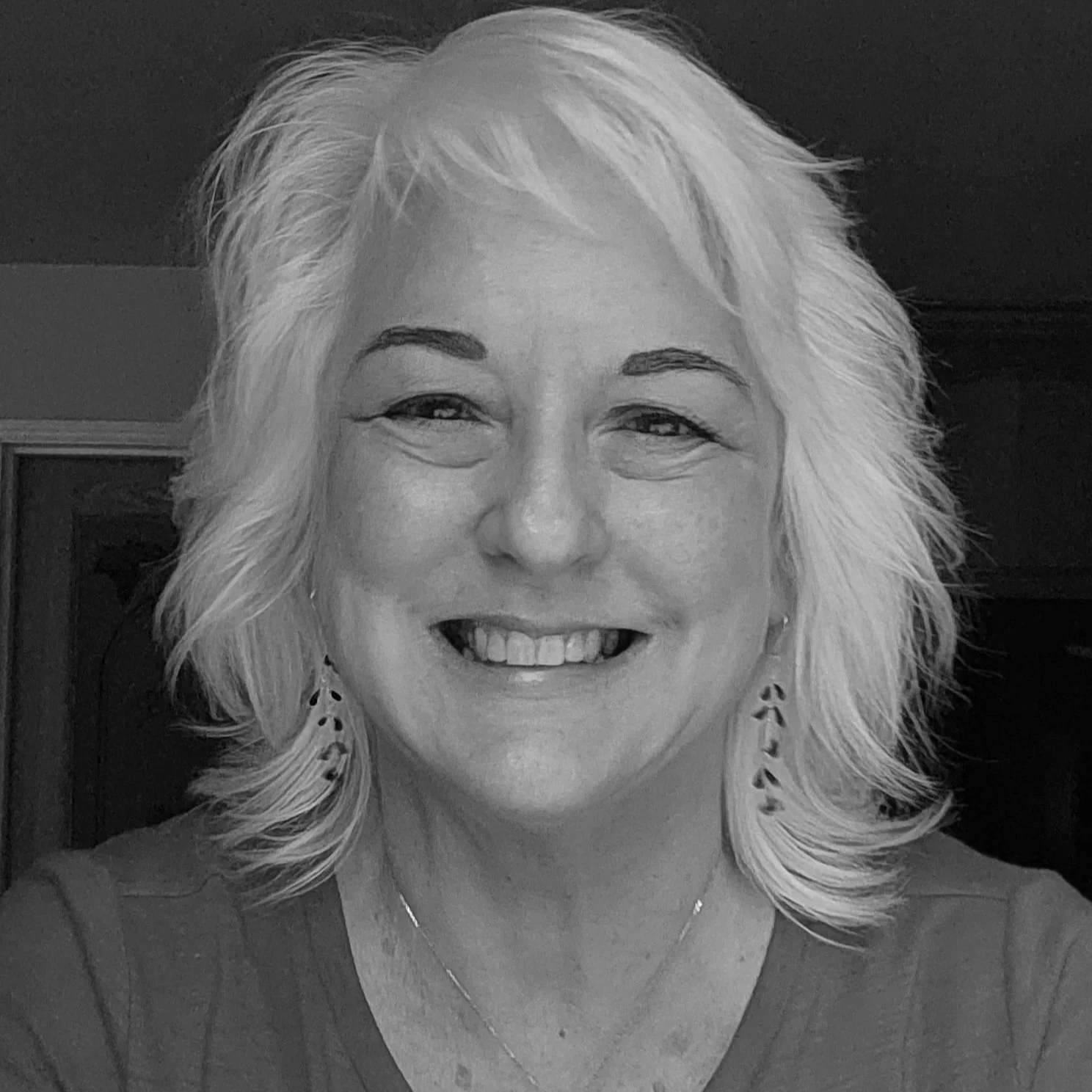 Black and white photo of smiling middle-aged woman with blonde hair, wearing earrings and a necklace.