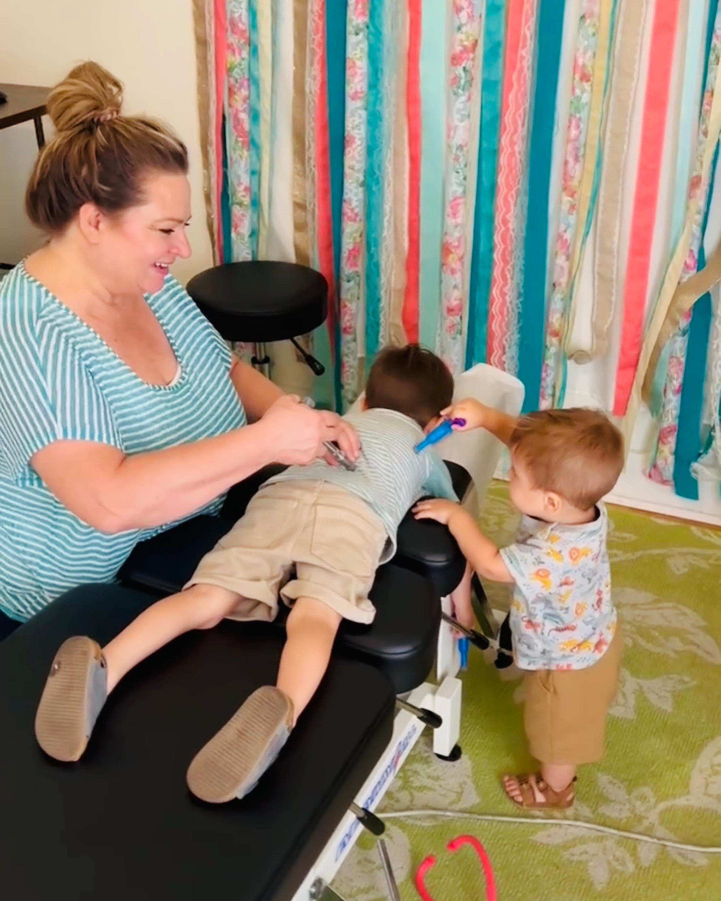 Chiropractor, Dr Leslie, at The Chiropractic Place for Mommy and Me in Aledo, TX  adjusting a child with his brother using a pretend activator