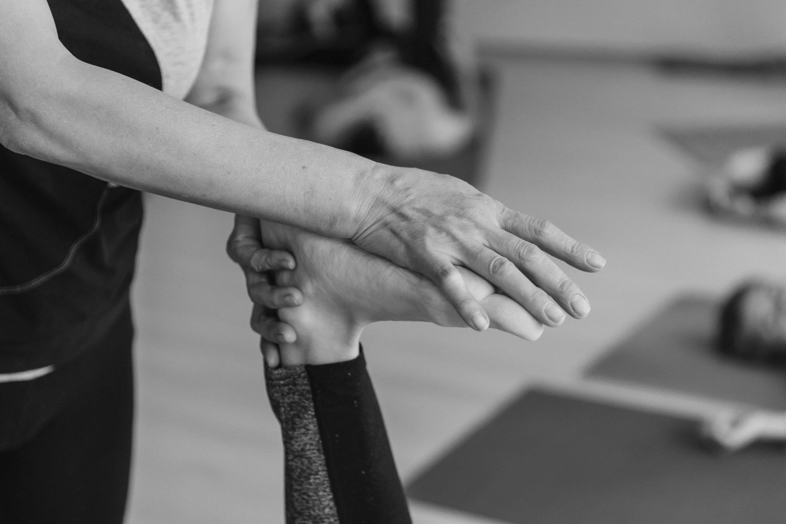 A person is helping an elderly individual stretch or do yoga, holding their hand and arm for support in a black-and-white photo.