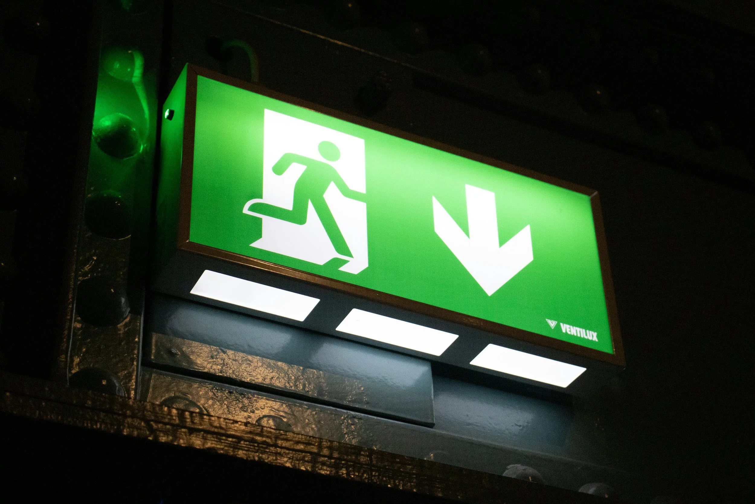 Green emergency exit sign with a running figure and downward arrow.