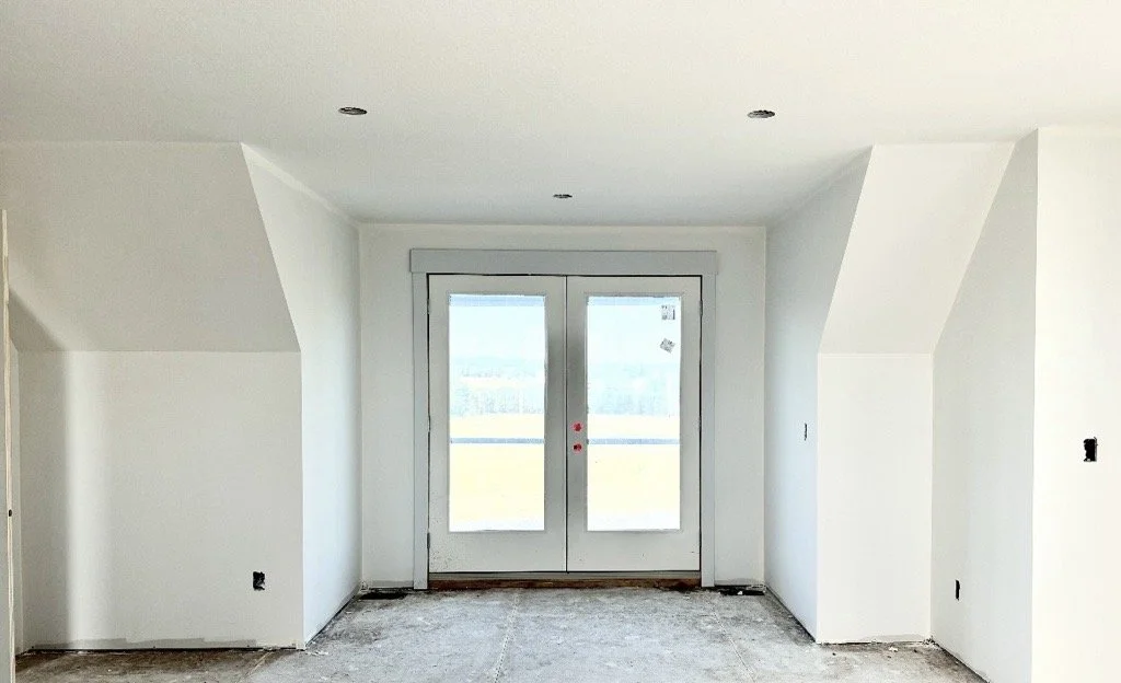 Empty room with white walls, a double glass door leading outside, and a unfinished floor.