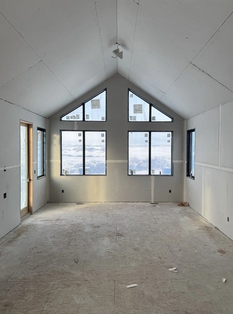 An unfinished room with large windows, a sloped ceiling, and a door on the left, in a building under construction.