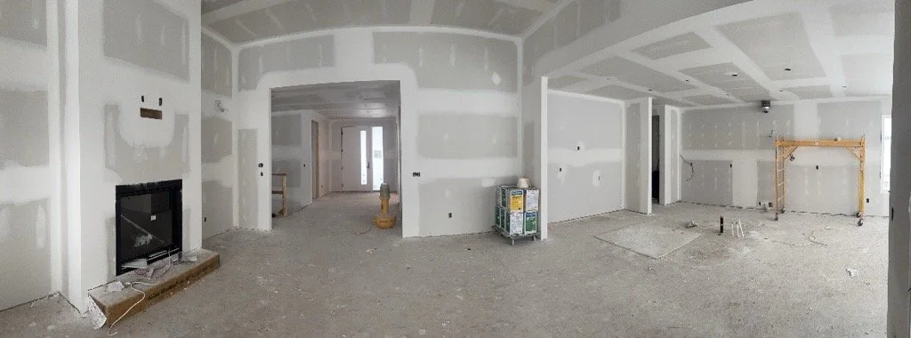 Interior of a house under construction with drywall installed, unfinished flooring, and building materials present.