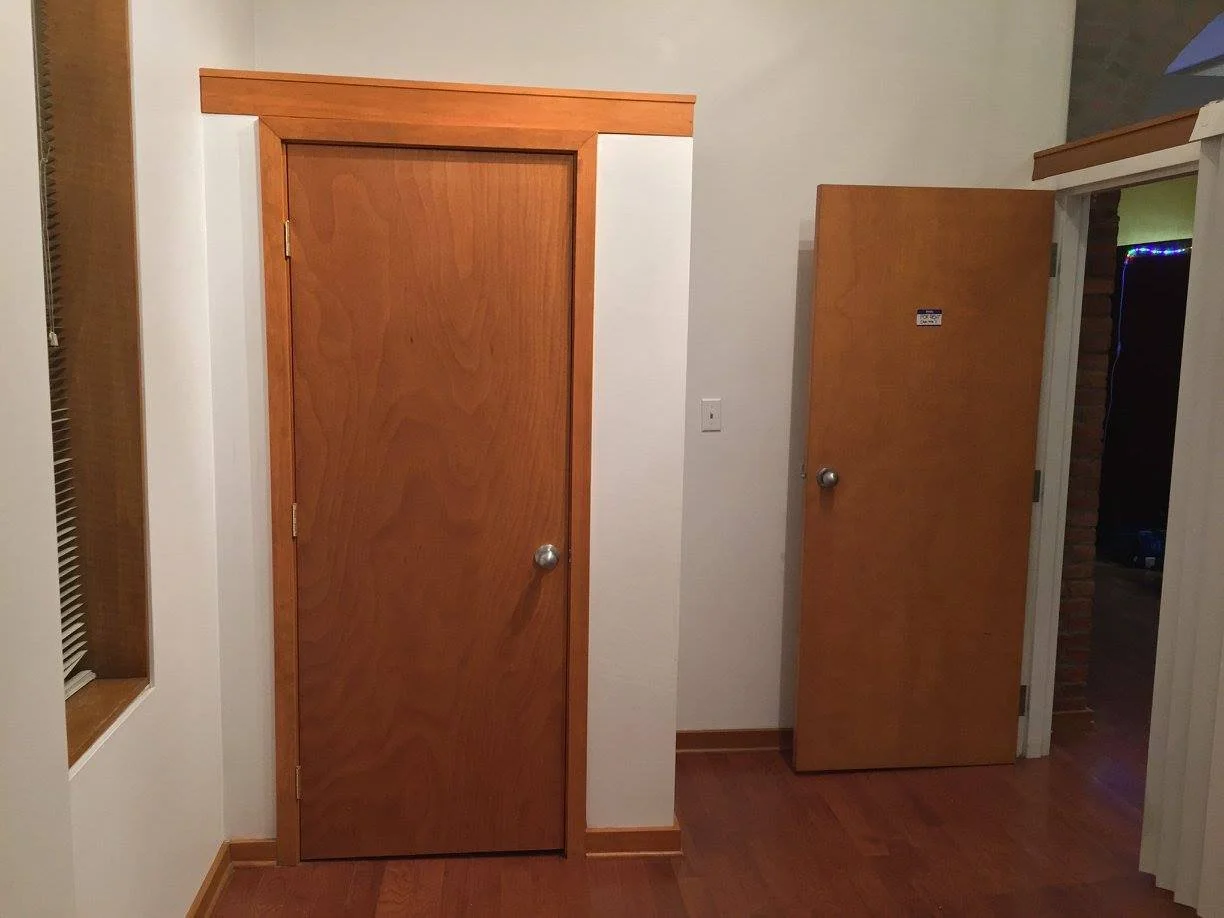 Two wooden doors, one closed and one open, in a room with wooden flooring and white walls.