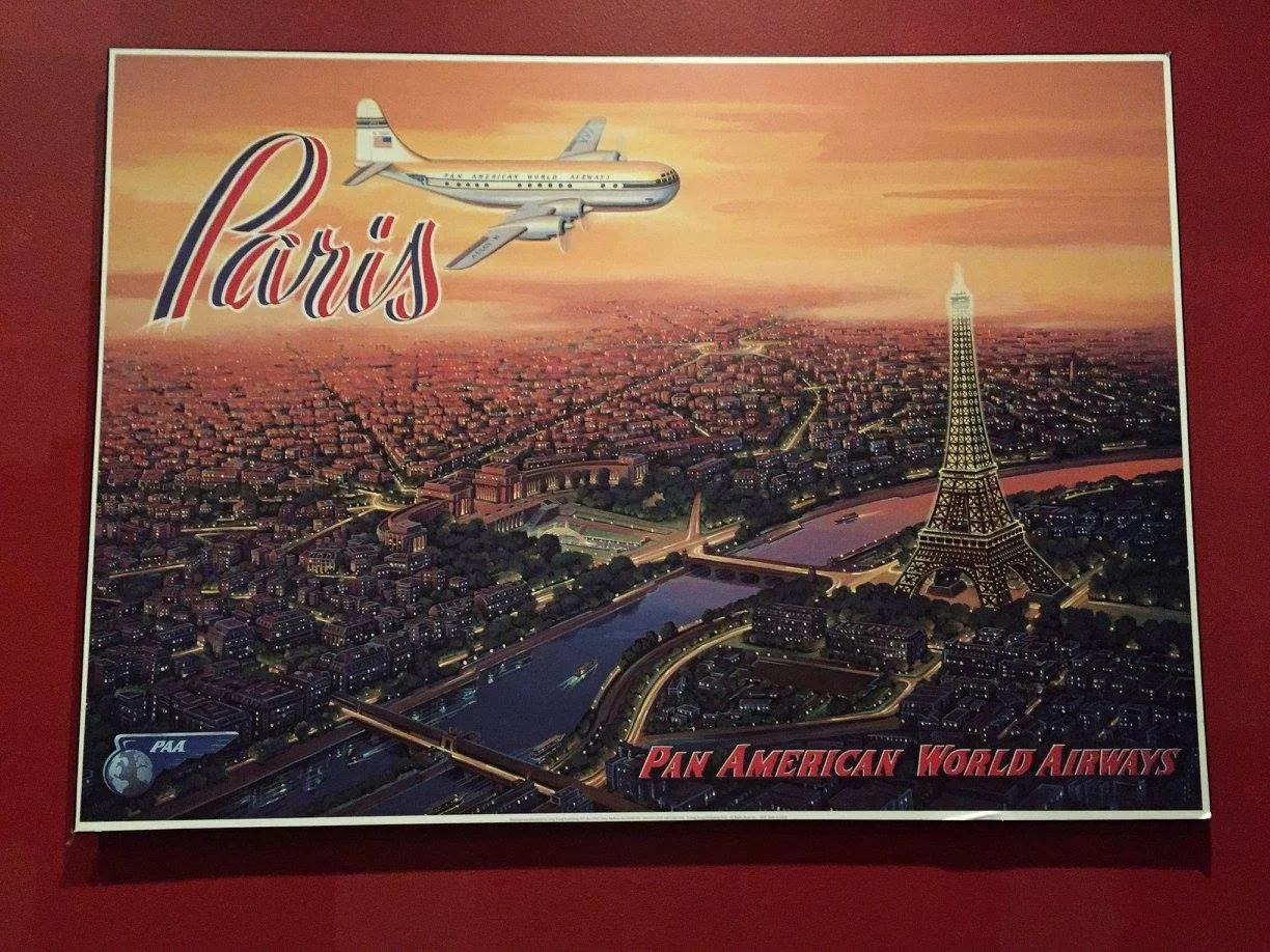 Illustration of Paris with the Eiffel Tower and an airplane flying overhead. The background features a sunset sky and an aerial view of the city with the Seine River. Text reads 'Paris' in large script and 'Pan American World Airways' at the bottom.