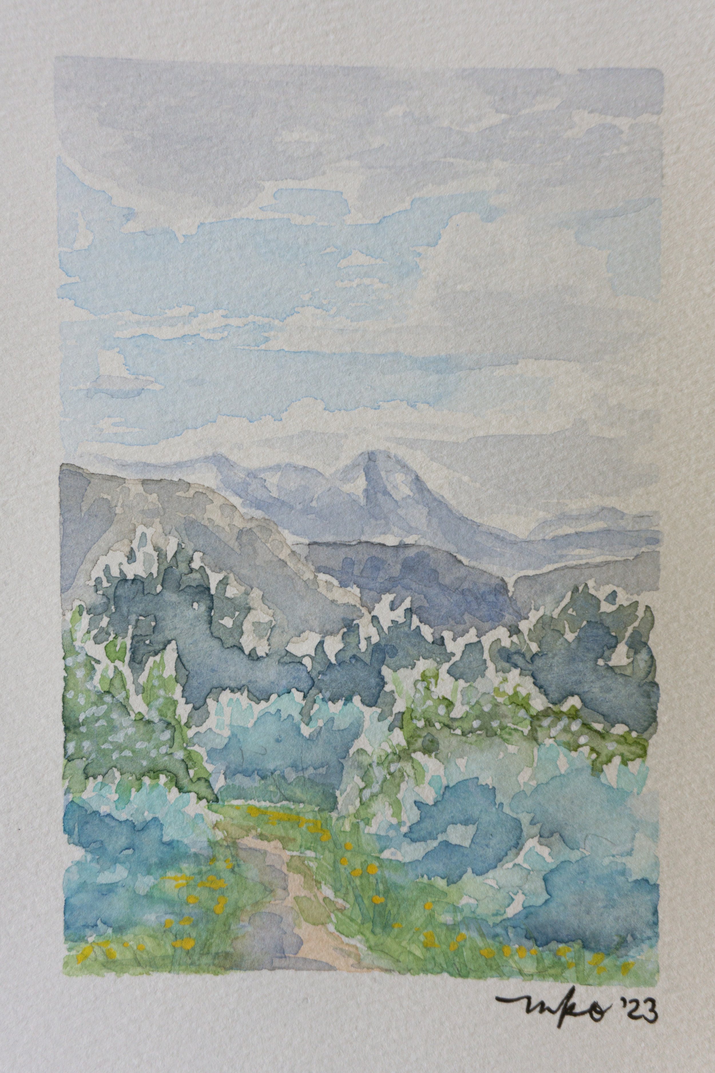 Watercolor painting showing a mountain landscape with a cloudy sky, green foliage, and a path through the grass.