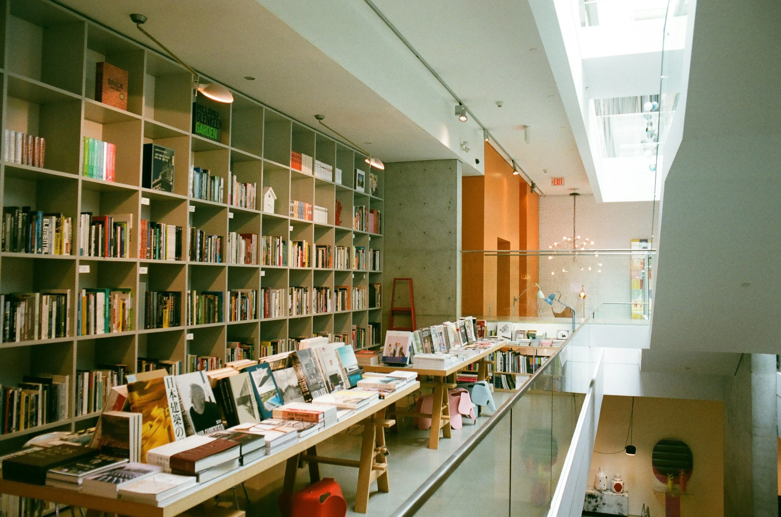 Modern bookstore interior with bookshelves and tables displaying books, featuring high ceilings and natural light.