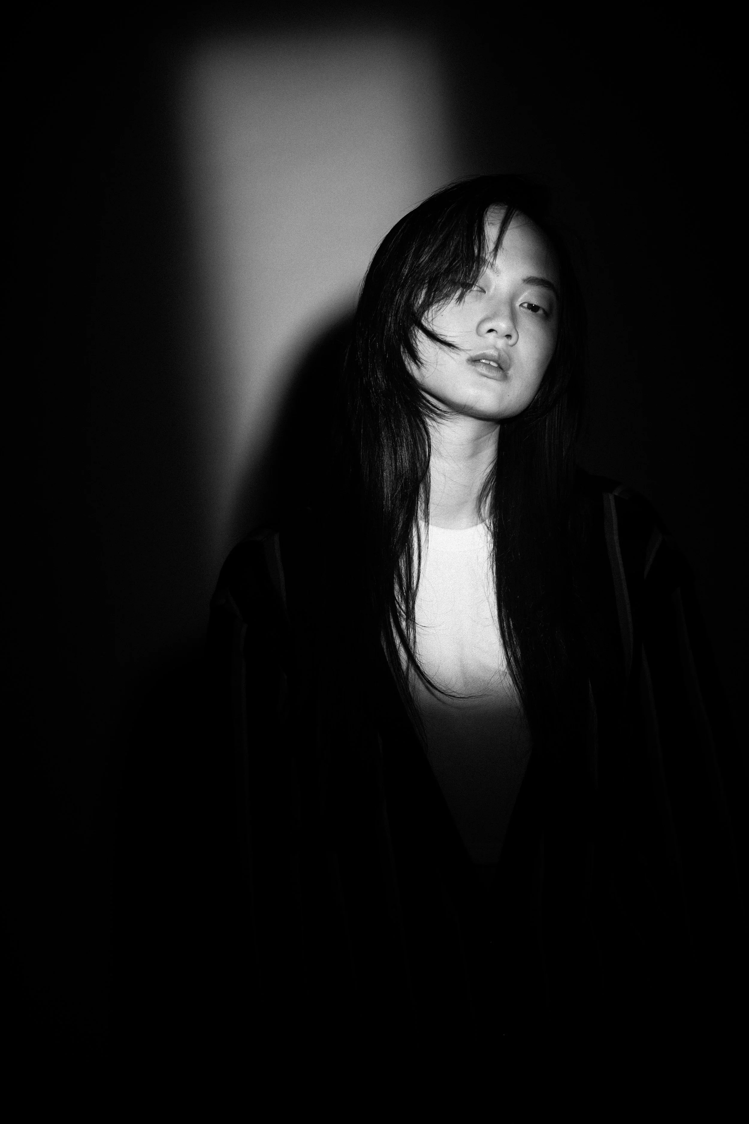 Black and white portrait of a woman with long dark hair, partially shadowed, looking at the camera with a calm expression.