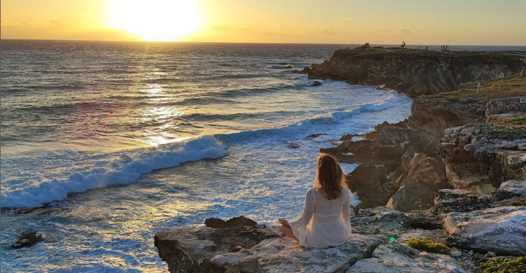 Edith en méditation sur des rochers, face à l’océan au coucher du soleil