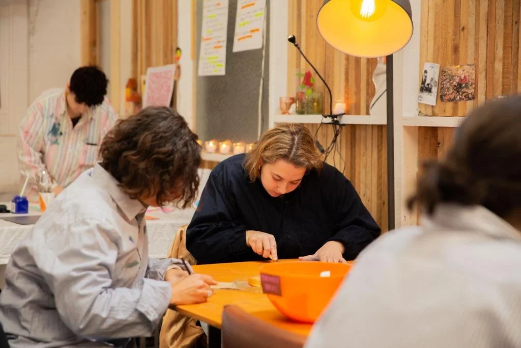 People engaged in an art or craft activity at a table in a cozy indoor setting with warm lighting and decorations.