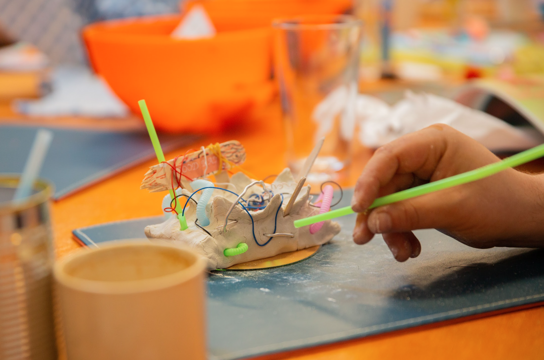 Close-up of a hand crafting with clay and colorful straws on a table.