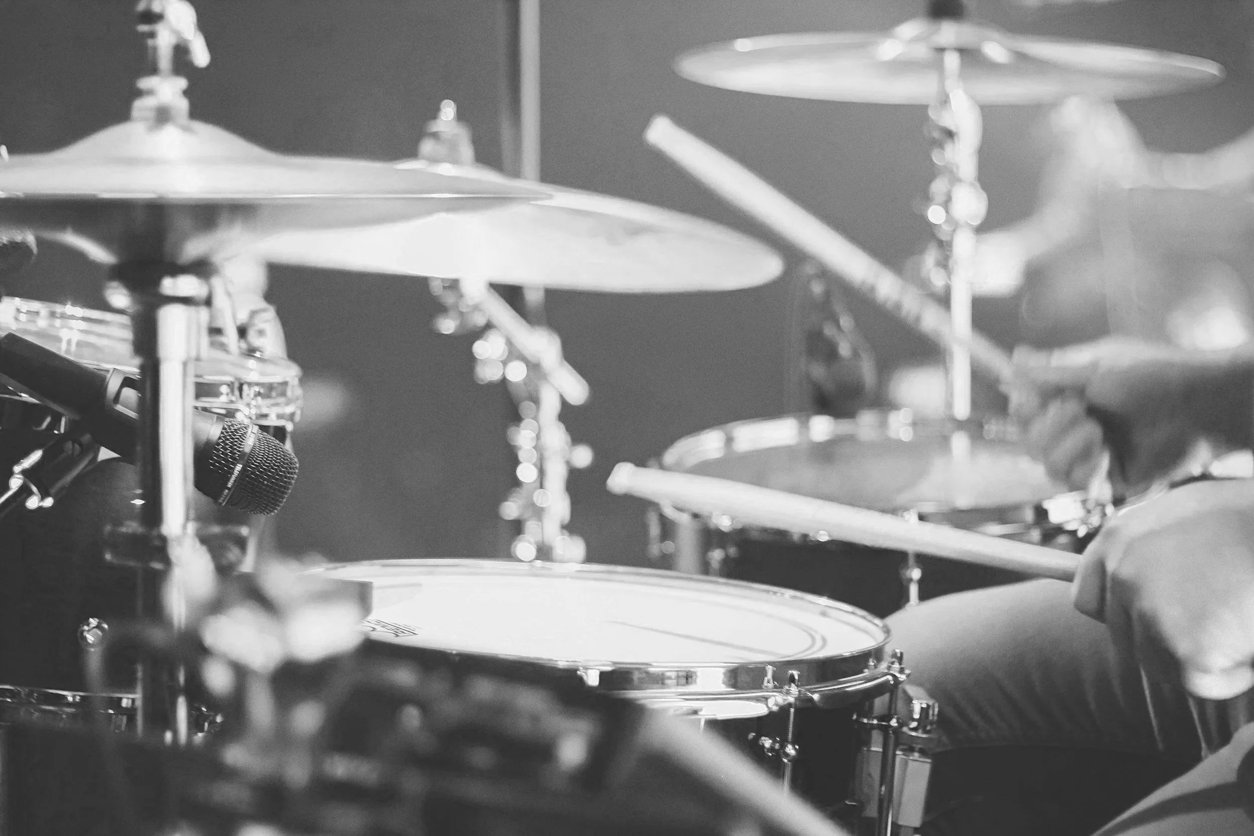 Close-up of a drummer playing drums on stage, with cymbals and drumsticks visible in black and white.