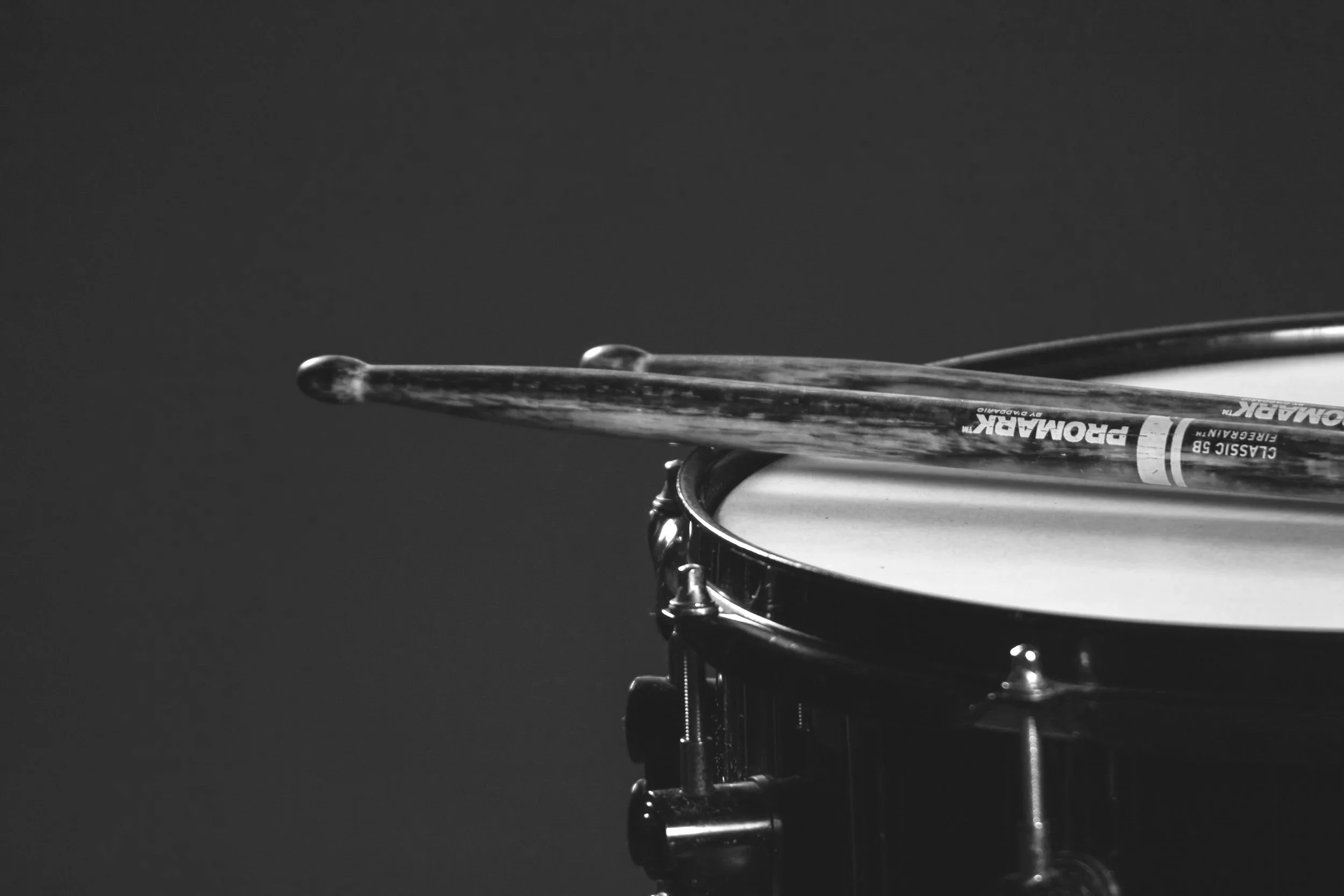 Black and white close-up of a snare drum with a drumstick resting on top.