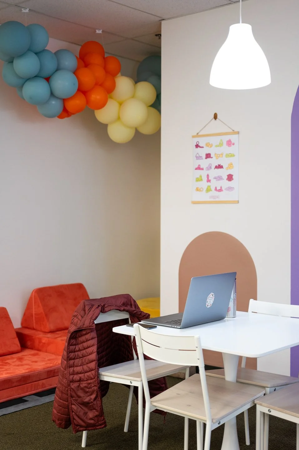 Inside Laro Tayo in the parent lounge area, a laptop sits on top of a table with a jacket on the chair, near the corner of soft play area of movable cushions