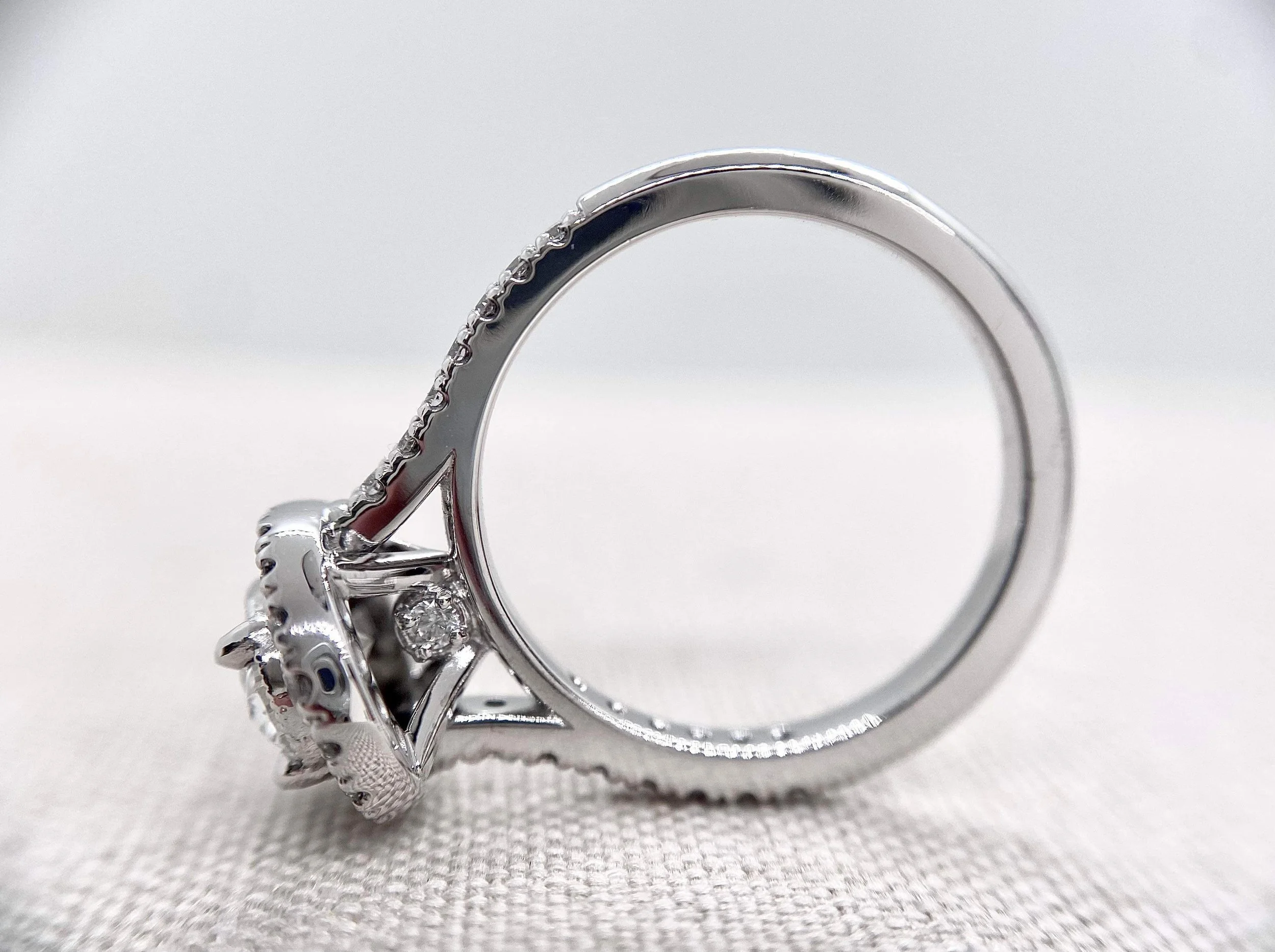 Side view of 18ct white gold engagement ring, oval centre stone, milgrain setting with hidden diamond setting.