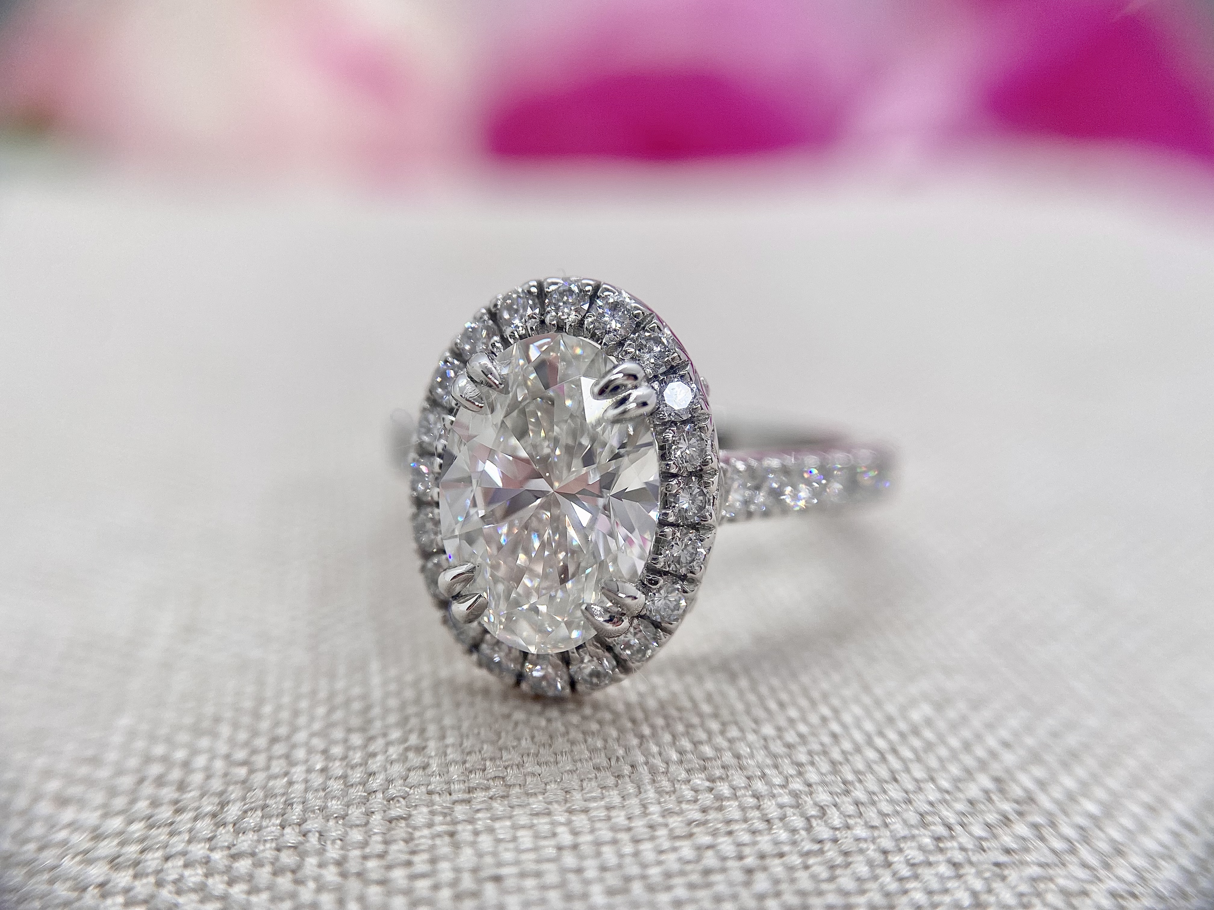 18ct white gold ring featuring a 2.04ct oval cut diamond set in double talon claws surrounded by French cut micro pave set round brilliant cut diamonds with a total weight of 0.87ct.