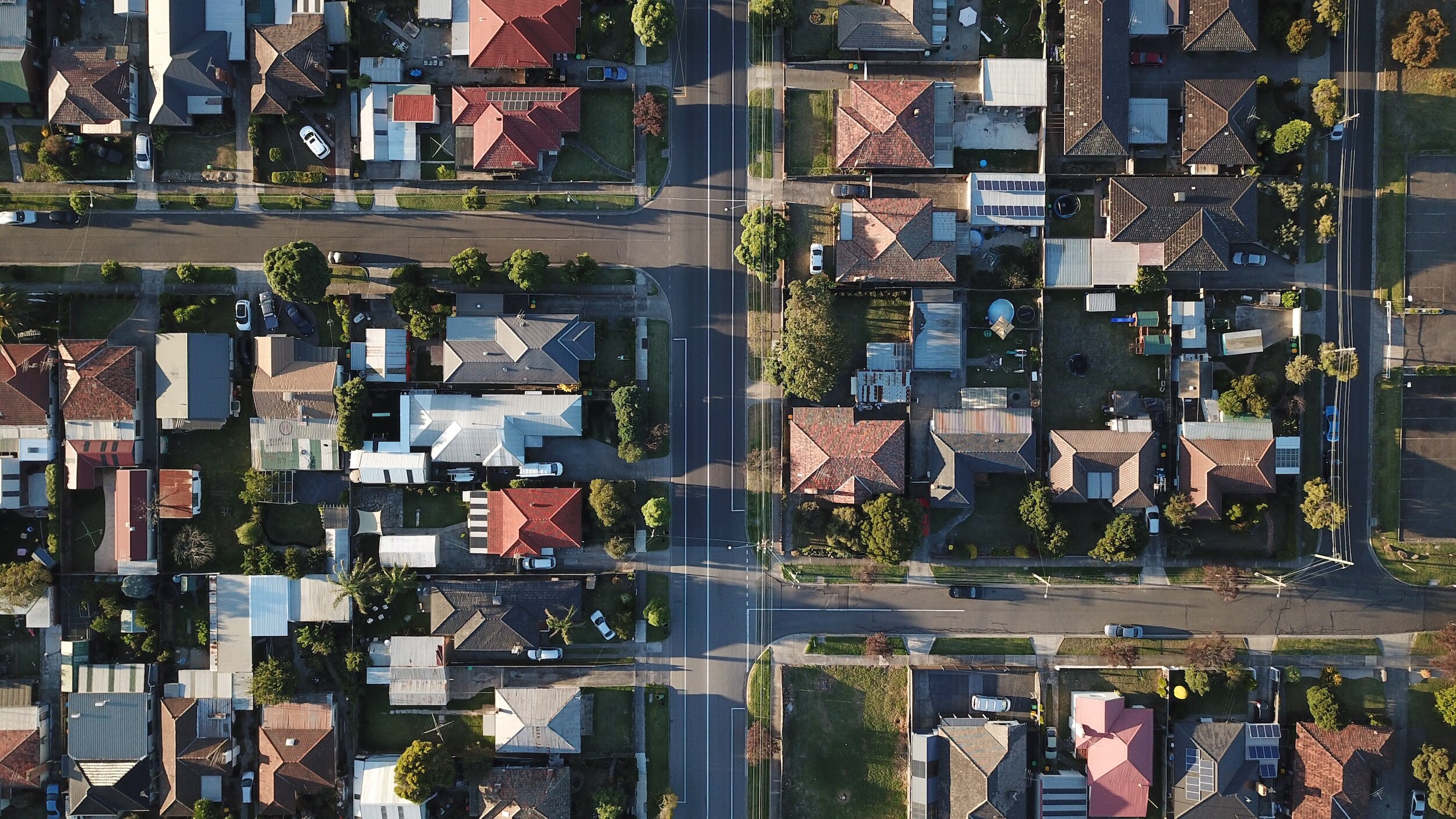 Aerial view of a suburban neighborhood with streets, houses, driveways, and greenery.