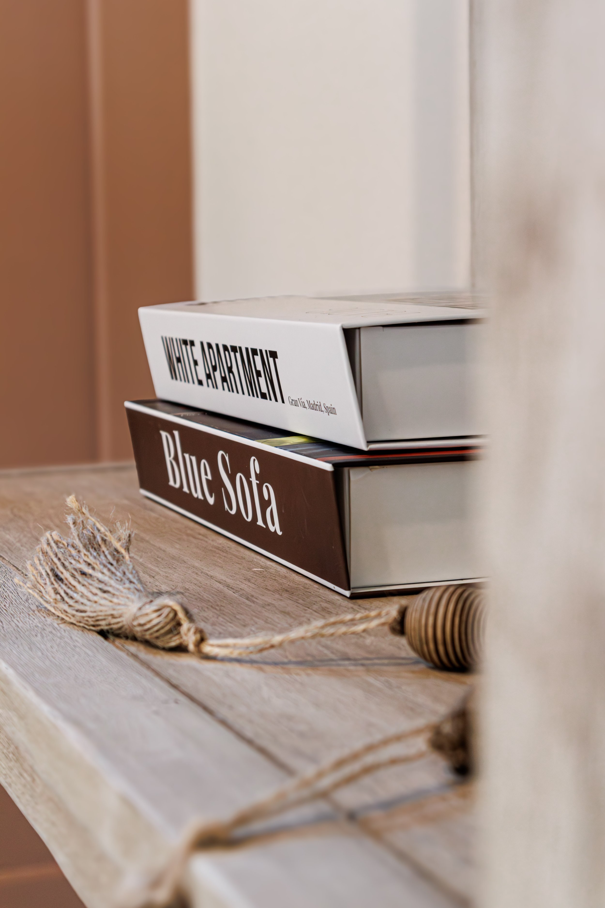 Stacked books titled "White Apartment" and "Blue Sofa" on a wooden surface with decorative tassels.