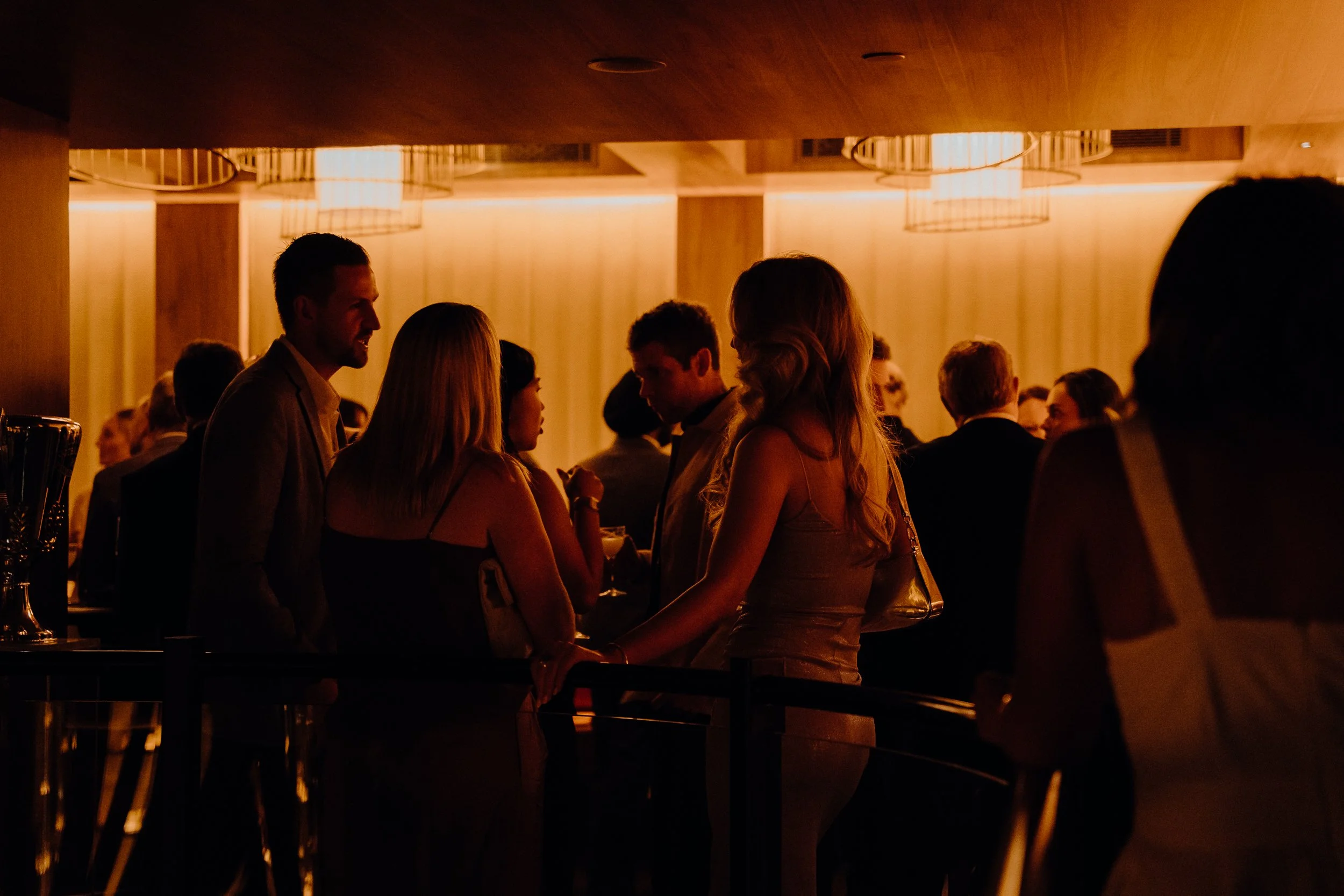 People socializing at a dimly lit event or party in a lounge or bar area.
