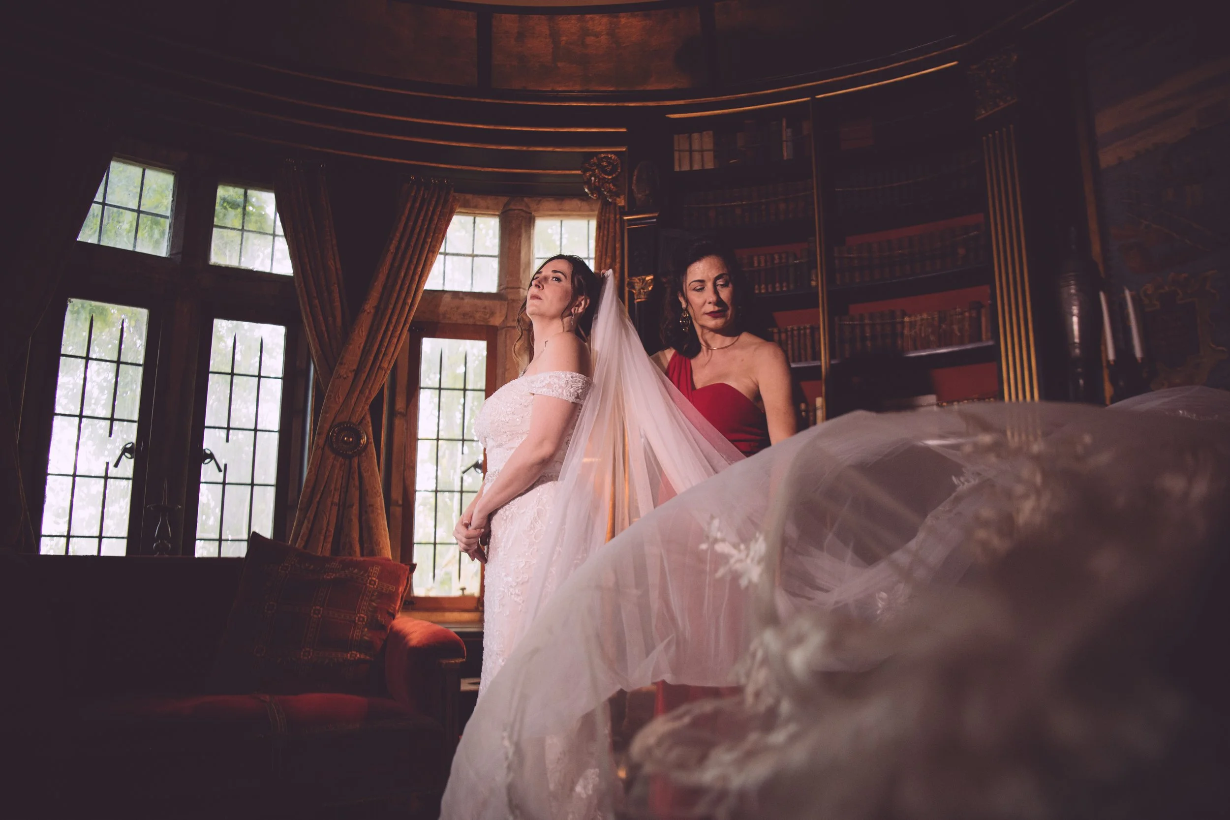 The bride's mother assisting with putting in the veil, as the final touch of her getting ready process, in an enchanting library of Hammond Castle in Gloucester, MA - Photography by Mike Indi