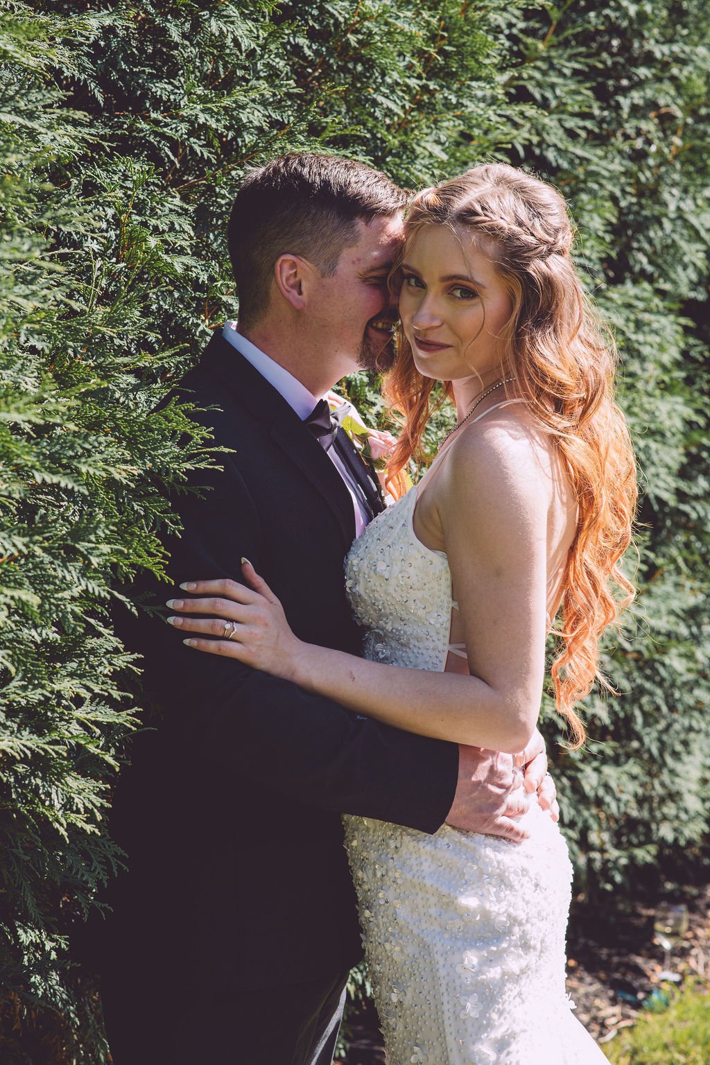 A groom whispering something to his beautiful bride during their sunny wedding day at Searles Chapel in Windham, NH. Photography by Mike Indi.