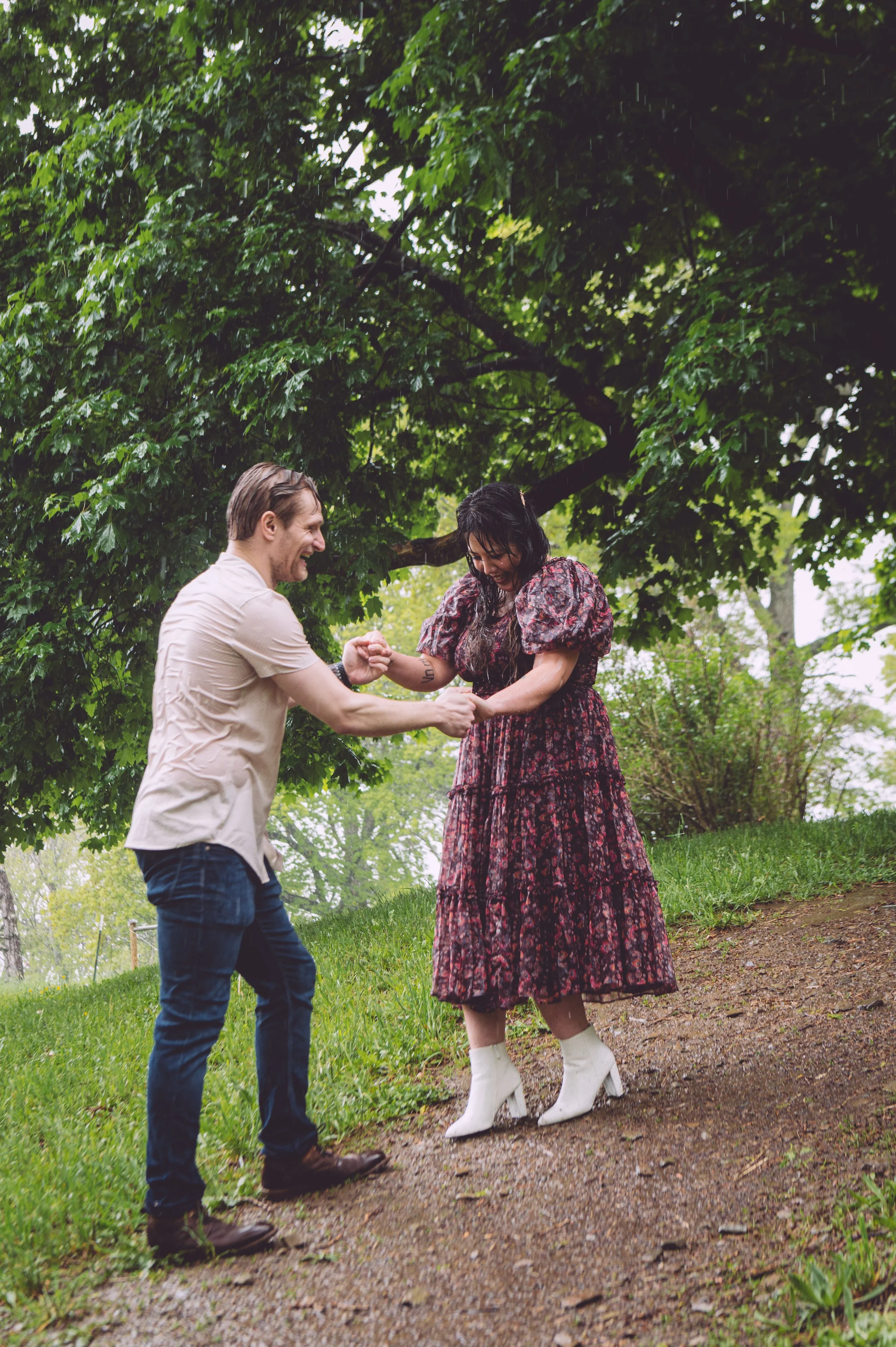 A groom being a gentleman by helping his bride walk through the rainy trail during their engagement session at Bancroft's Castle in Groton, MA. Engagement photography by Mike Indi.