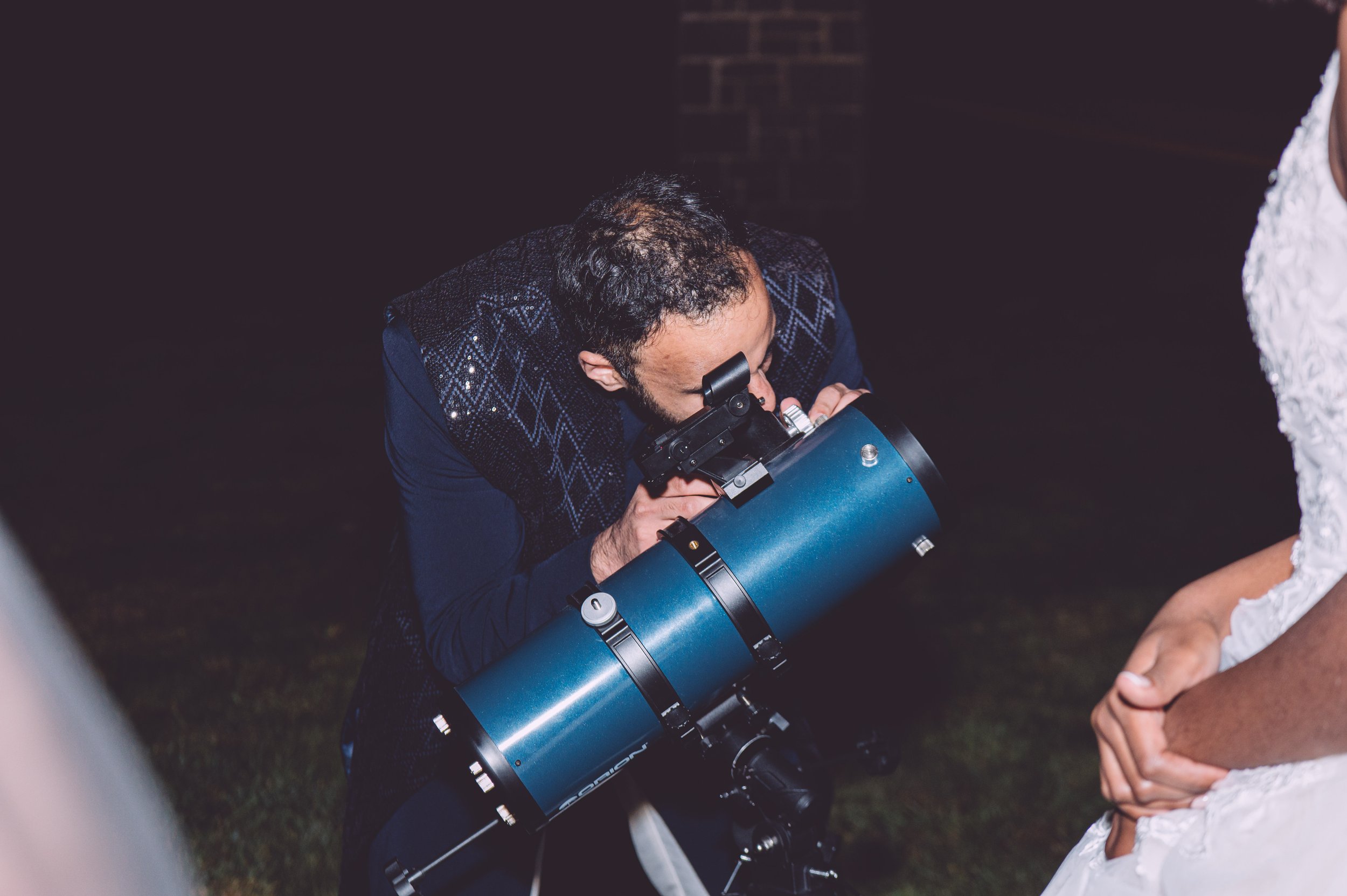 A groom making adjustments to his telescope to view Saturn in the clear night sky during his fall wedding at Searles Chapel in Windham, NH. Wedding photography by Mike Indi.