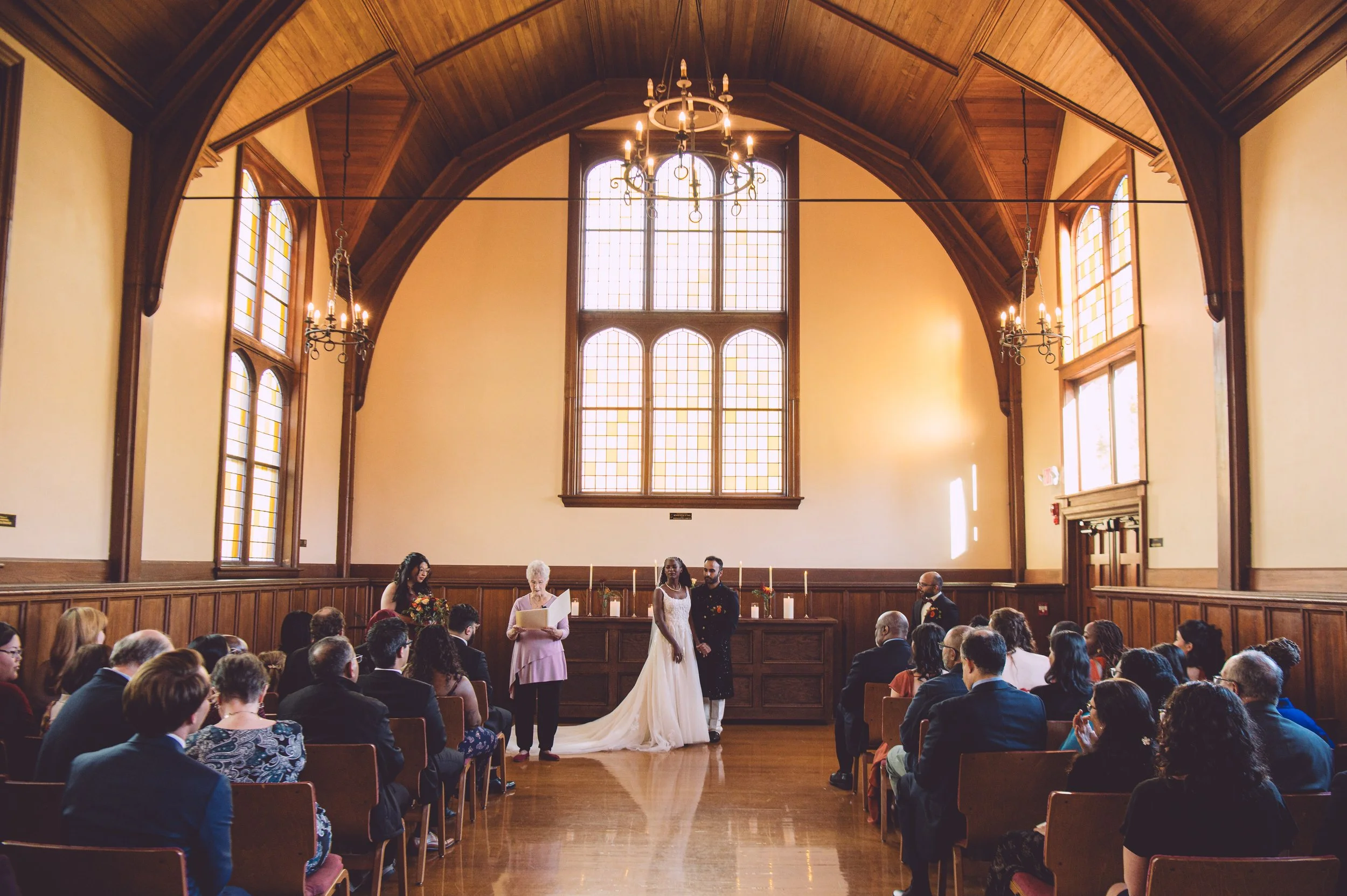 A bride and groom holding hands during their wedding ceremony at Searles Chapel in Windham, NH. Wedding photography by Mike Indi.