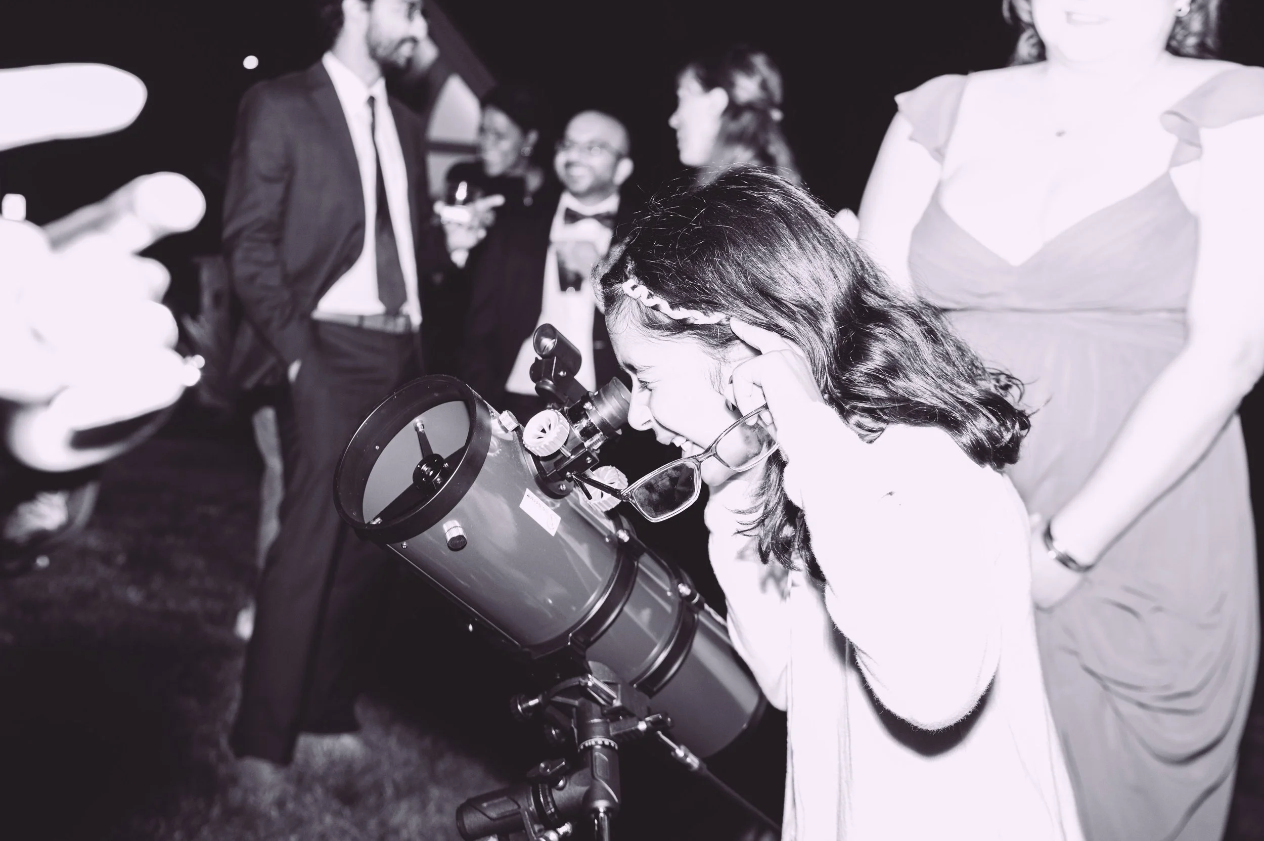 Wedding guests looking through a telescope to view Saturn during a wedding reception at Searles Chapel in Windham, NH. Wedding photography by Mike Indi.