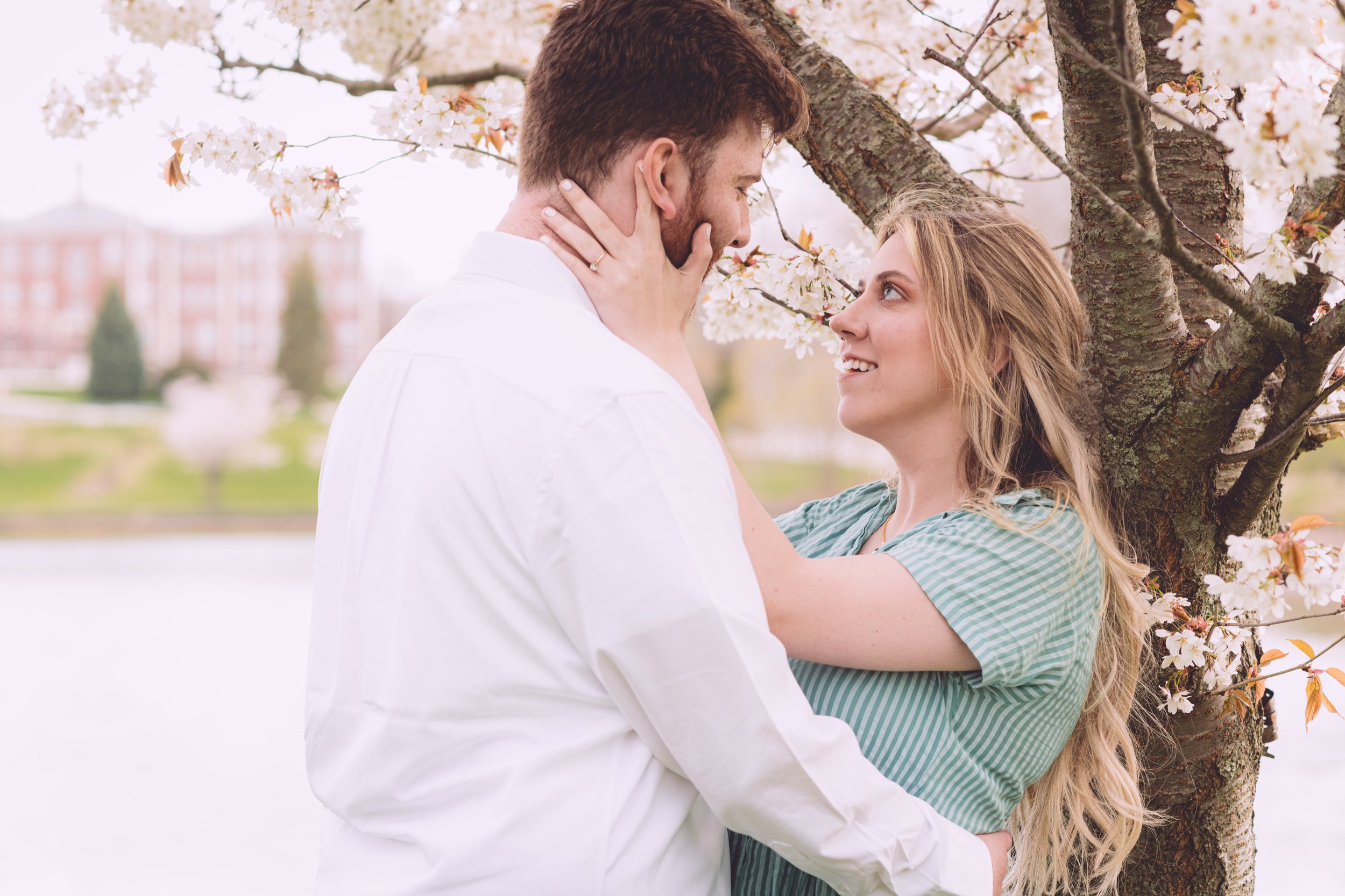 Hannah and Ben sharing a romantic embrace under a blooming tree during their engagement session in Portsmouth, NH - Photography by Mike Indi