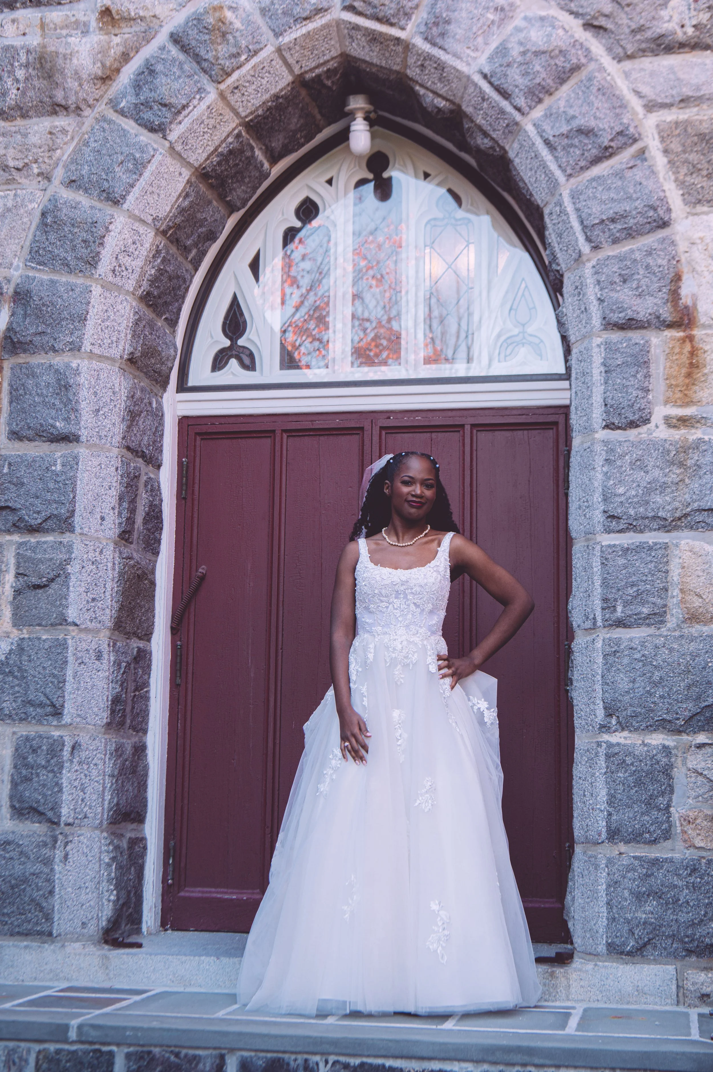 A stunning bride under a stone archway heading to see her groom for their first look before their wedding at Searles Chapel in Windham, NH. Wedding photography by Mike Indi.