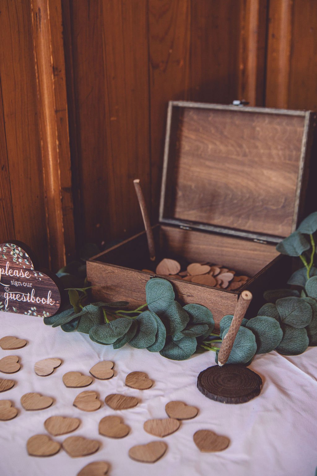 Small wooden hearts spread across a table with a box full of the hearts in the background for guests to sign and send love notes to the bride and groom during their wedding at Searles Chapel in Windham, NH. Wedding photography by Mike Indi.