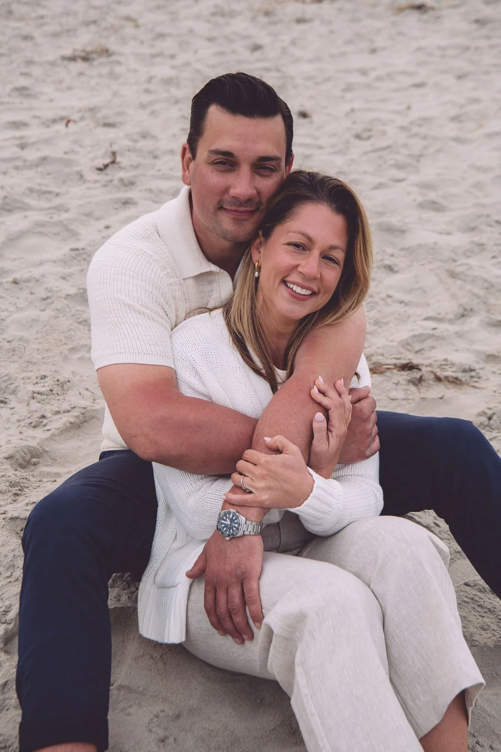 Amanda and Christopher wrapped in each other's arms while cuddling on the beach during their summer engagement session in Ogunquit, ME. Photography by Mike Indi.