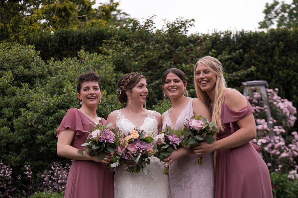 A stunning bride laughing with her beautiful bridesmaids during her wedding at the Gardens at Uncanoonuc in Goffstown, NH. Photography by Mike Indi.