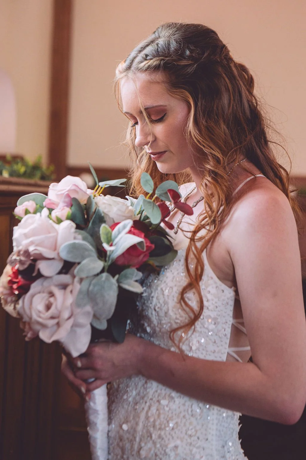 A beautiful bride lifting her bouquet of pink rose and smelling her wedding flowers before her wedding at Searles Chapel in Windham, NH. Wedding photography by Mike Indi.