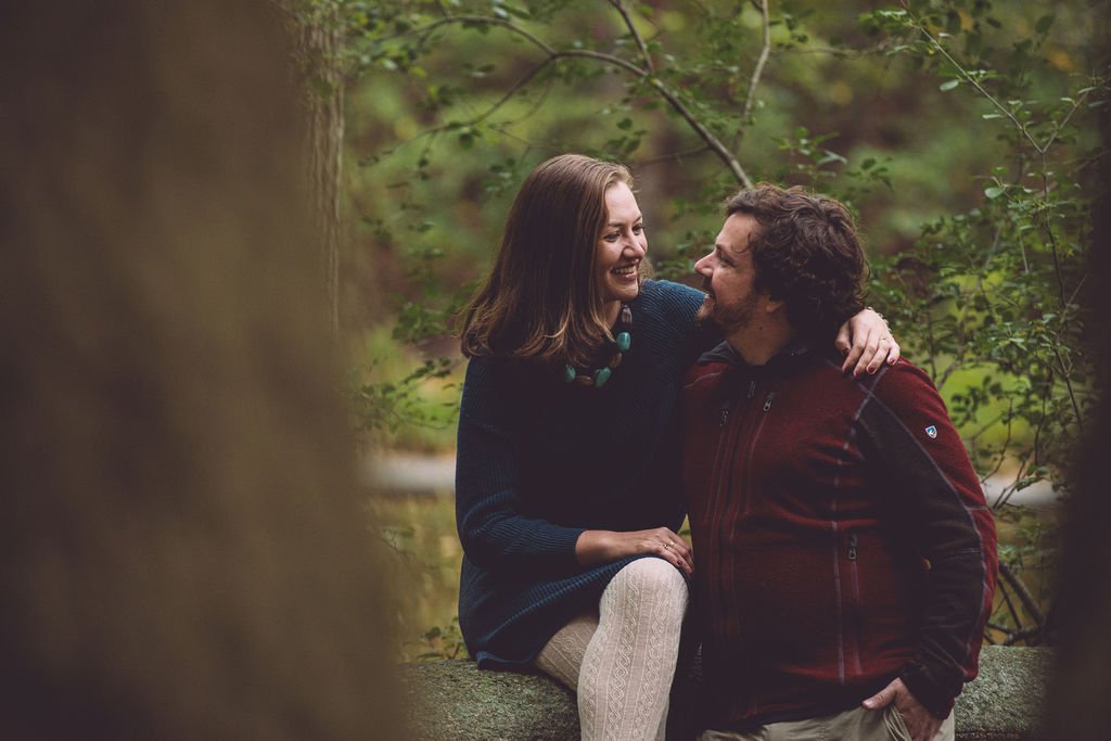 Meg and Stephen in a warm and loving embrace while sitting on a bridge during their fall engagement session in Olmsted Park in Boston, MA. Photography by Mike Indi.