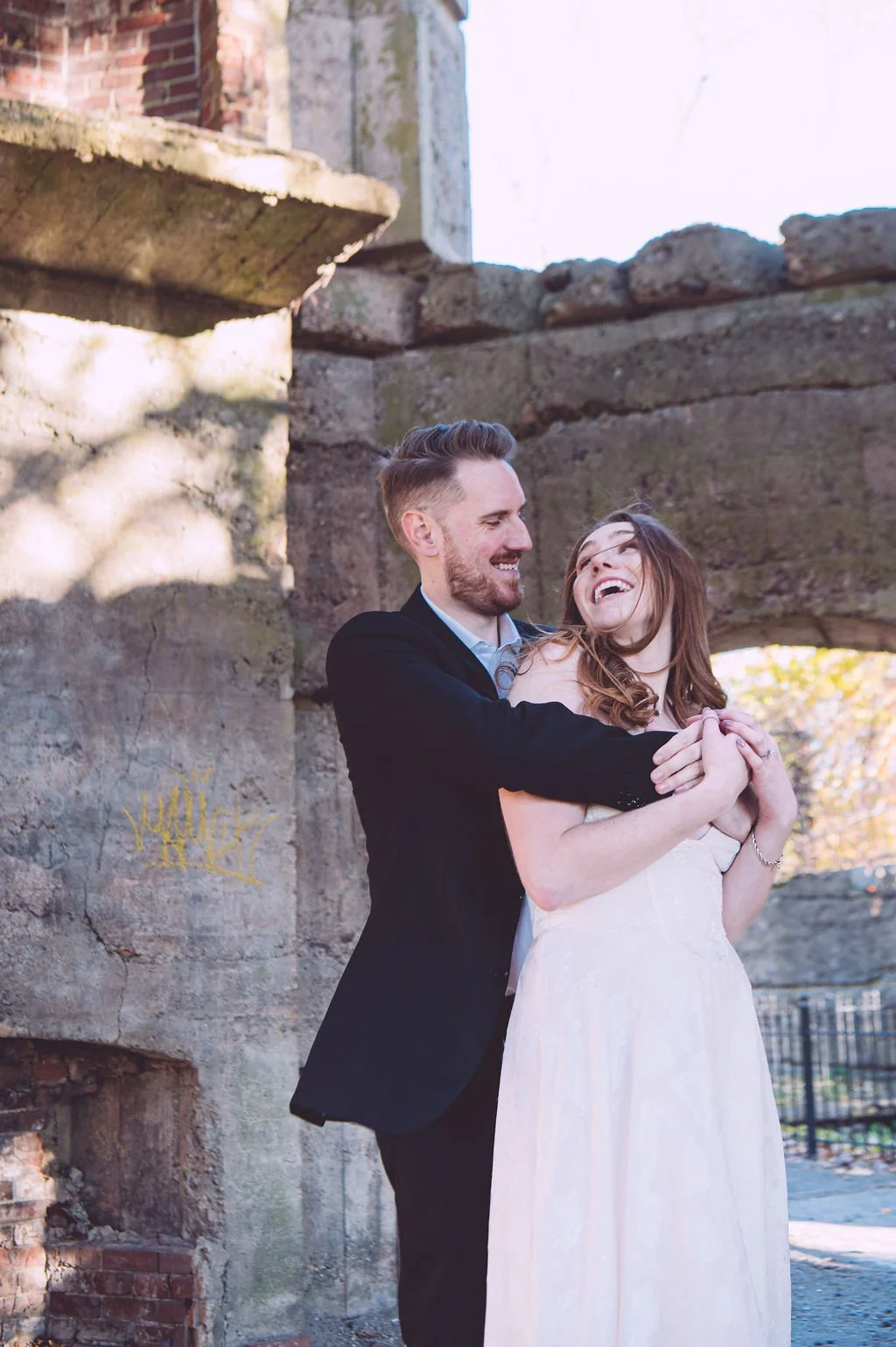 A happy bride smiling while being hugged by her groom during their engagement session at Bancroft's Castle in Groton, MA. Engagement photography by Mike Indi.