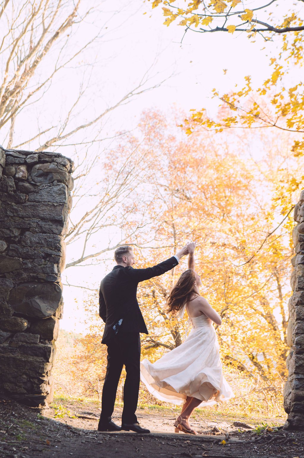 A bride and groom dancing and twirling between the stone ruins of Bancroft's Castle in Groton, MA. Engagement photography by Mike Indi.